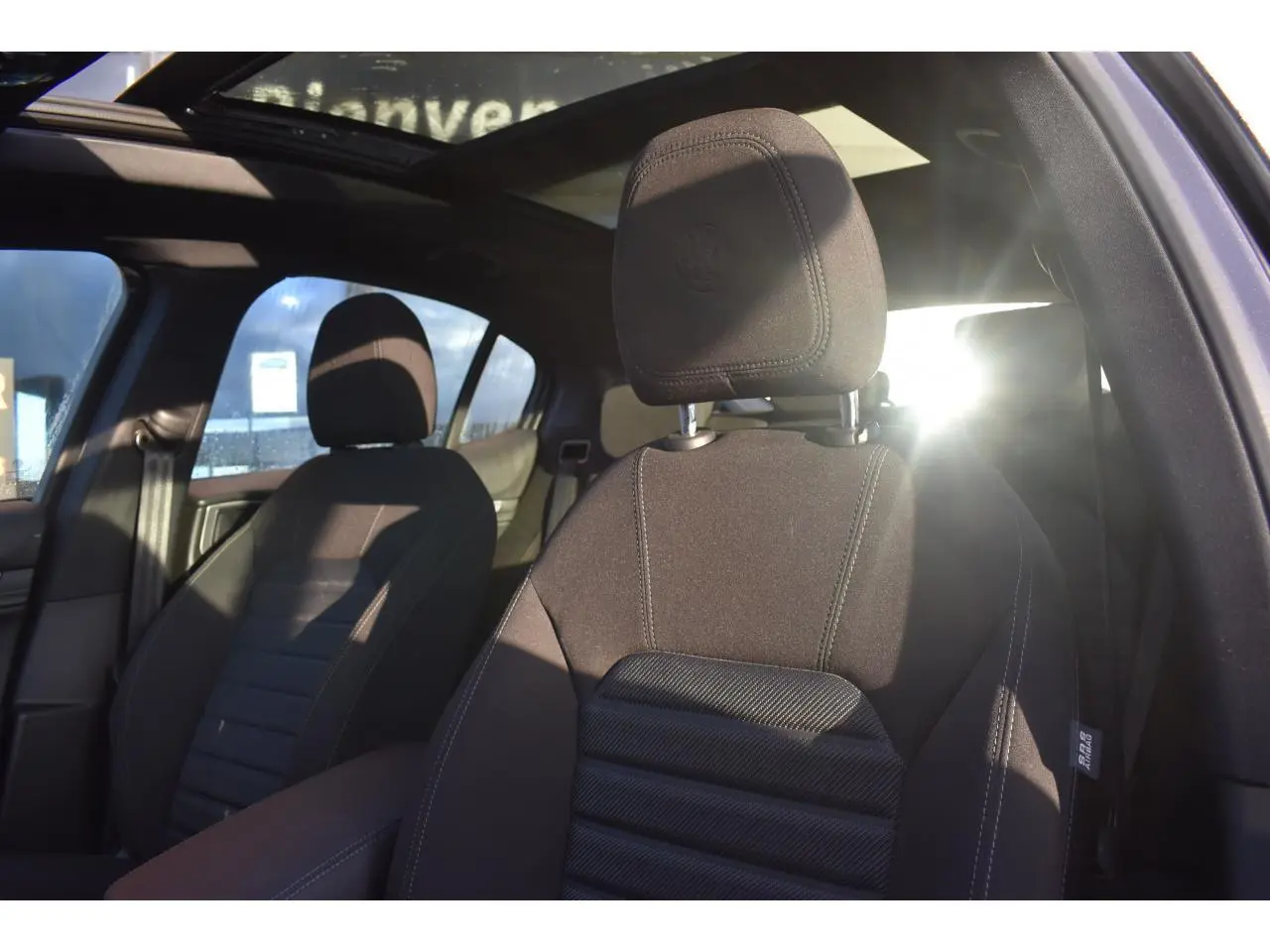 Vue intérieure de l'Alfa Romeo Stelvio 2024 montrant les sièges avant noirs et le toit ouvrant panoramique.