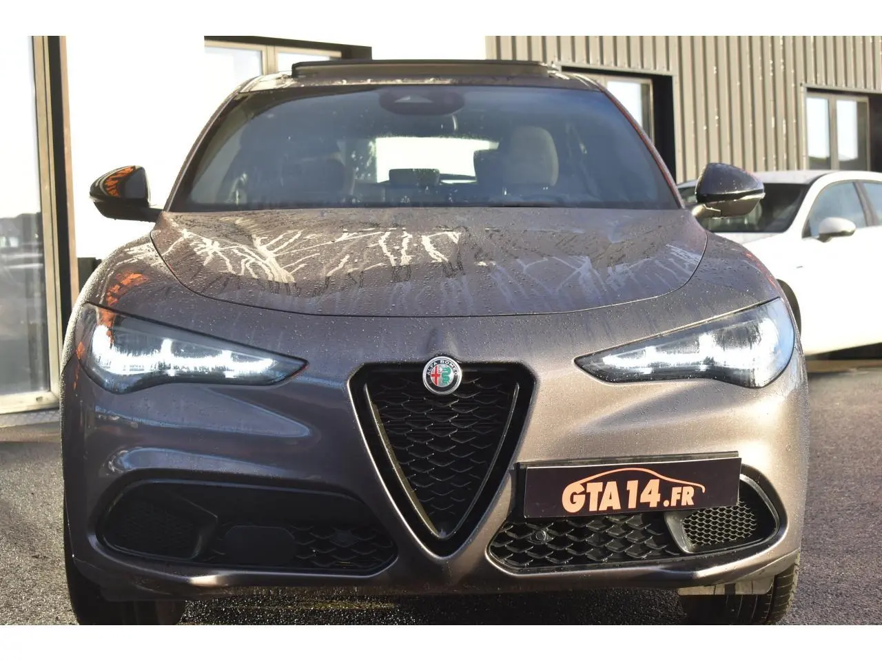 Vue avant d'un Alfa Romeo Stelvio 2024 gris Vesuvio métallisé avec feux LED allumés et calandre caractéristique en V.