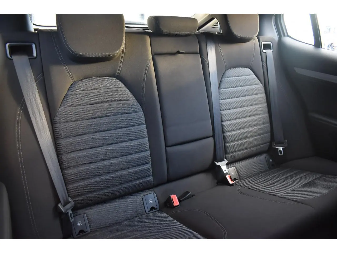 Vue intérieure sur les sièges arrière noirs en tissu et cuir de l'Alfa Romeo Stelvio 2024, avec ceintures de sécurité visibles.