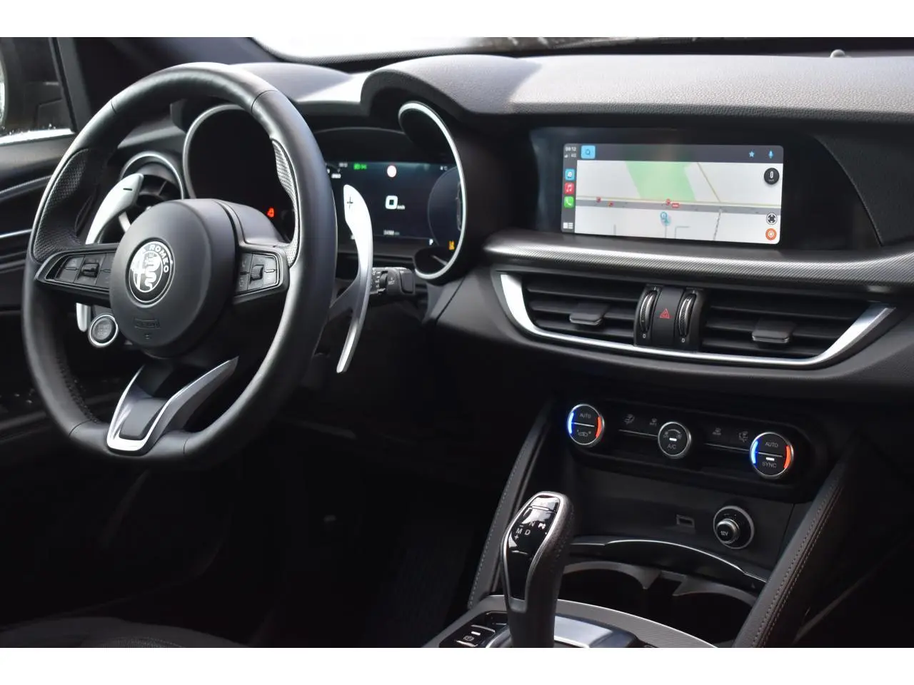 Intérieur de l'Alfa Romeo Stelvio 2024 vu côté conducteur, tableau de bord noir avec écran tactile et volant sport.