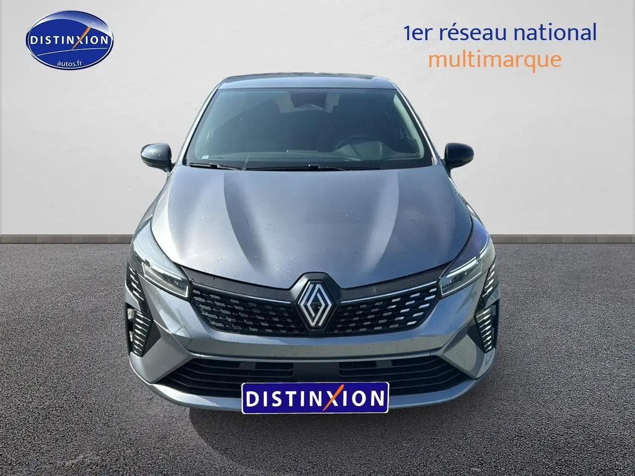 Vue avant d'une Renault Clio V gris schiste avec calandre chromée et phares LED allumés sur fond neutre.