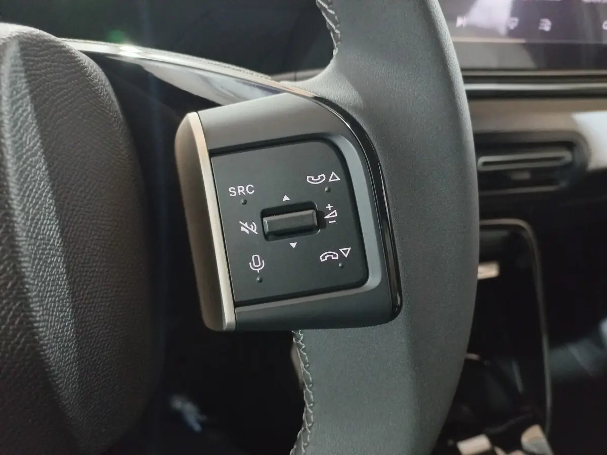 Gros plan sur les commandes gauche du volant cuir gris foncé de la Citroën C3 hybride 2025, avec boutons multifonctions.