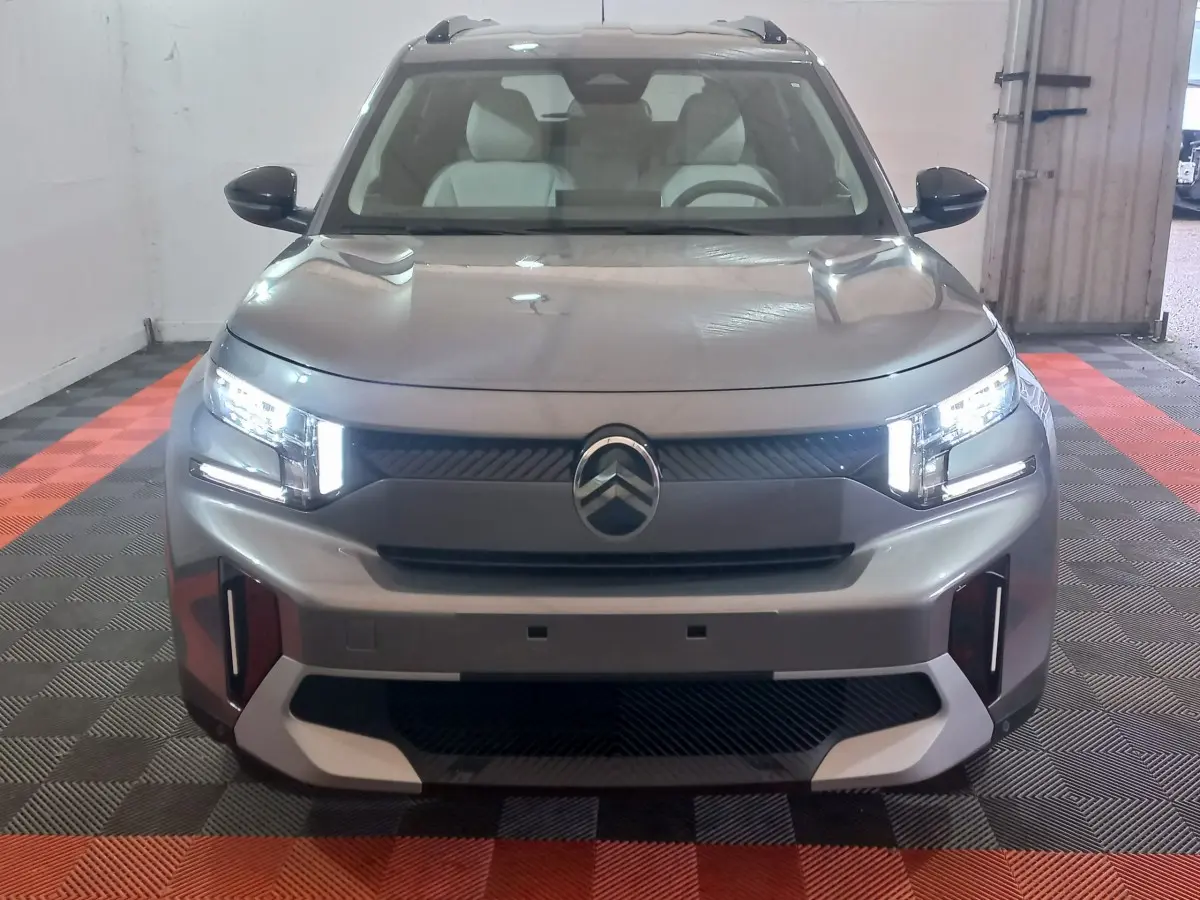 Vue frontale d'une Citroën C3 hybride gris foncé avec phares LED allumés dans un garage.