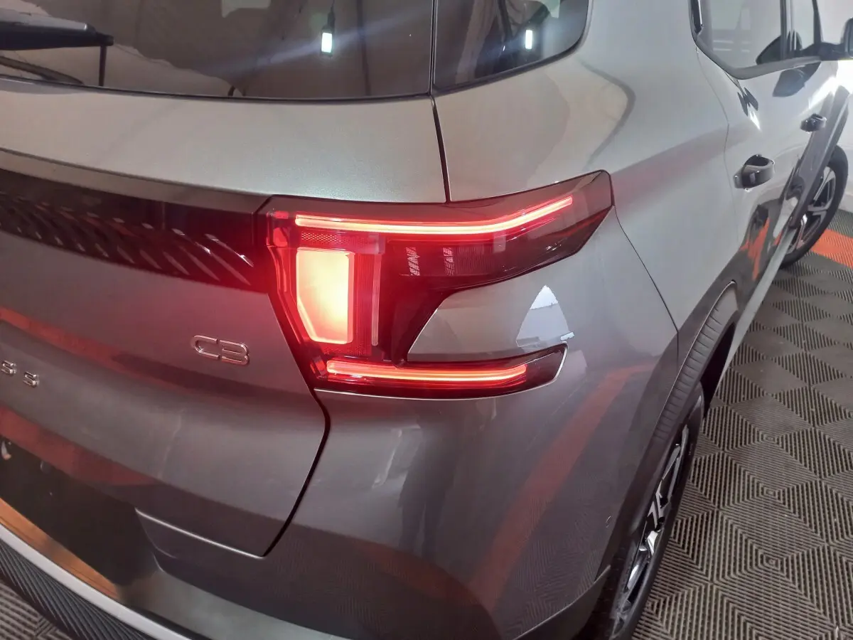 Feu arrière droit allumé d'une Citroën C3 hybride gris foncé vue en 3/4 arrière droit sur sol à motifs.