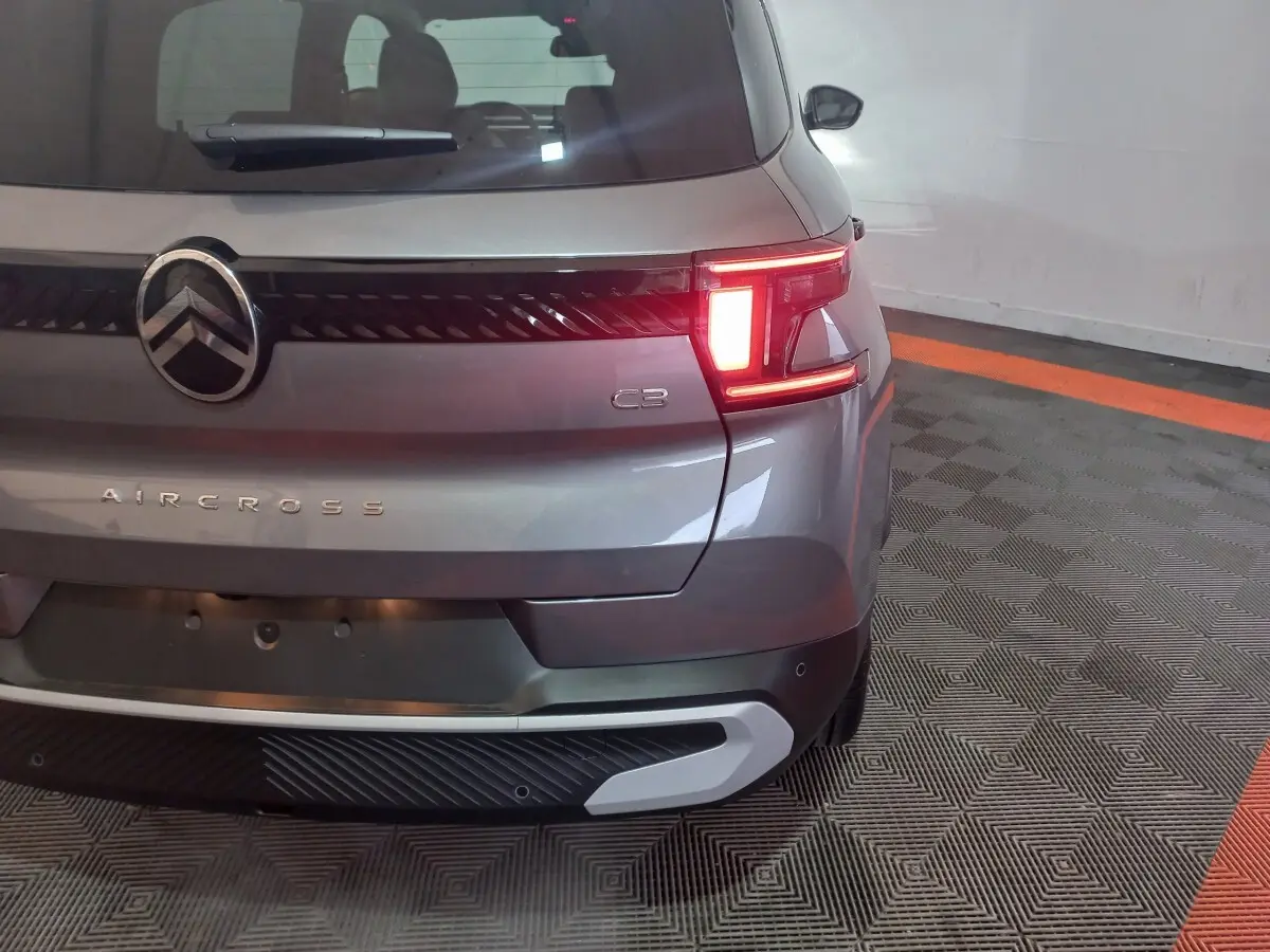 Vue arrière droite d'une Citroën C3 Aircross gris foncé avec feux arrière allumés dans un garage.