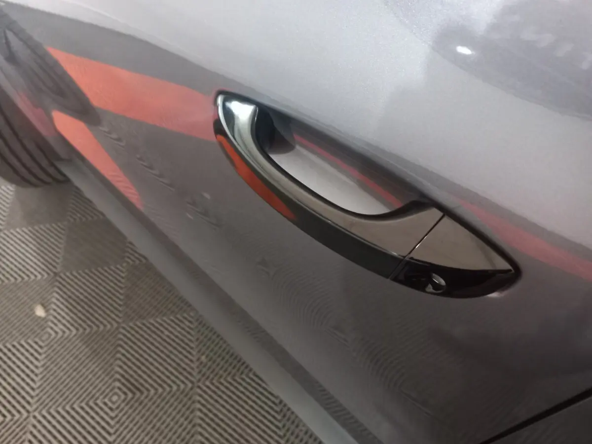 Poignée de porte côté gauche sur Citroën C3 hybride gris foncé, vue rapprochée mettant en valeur la finition brillante.