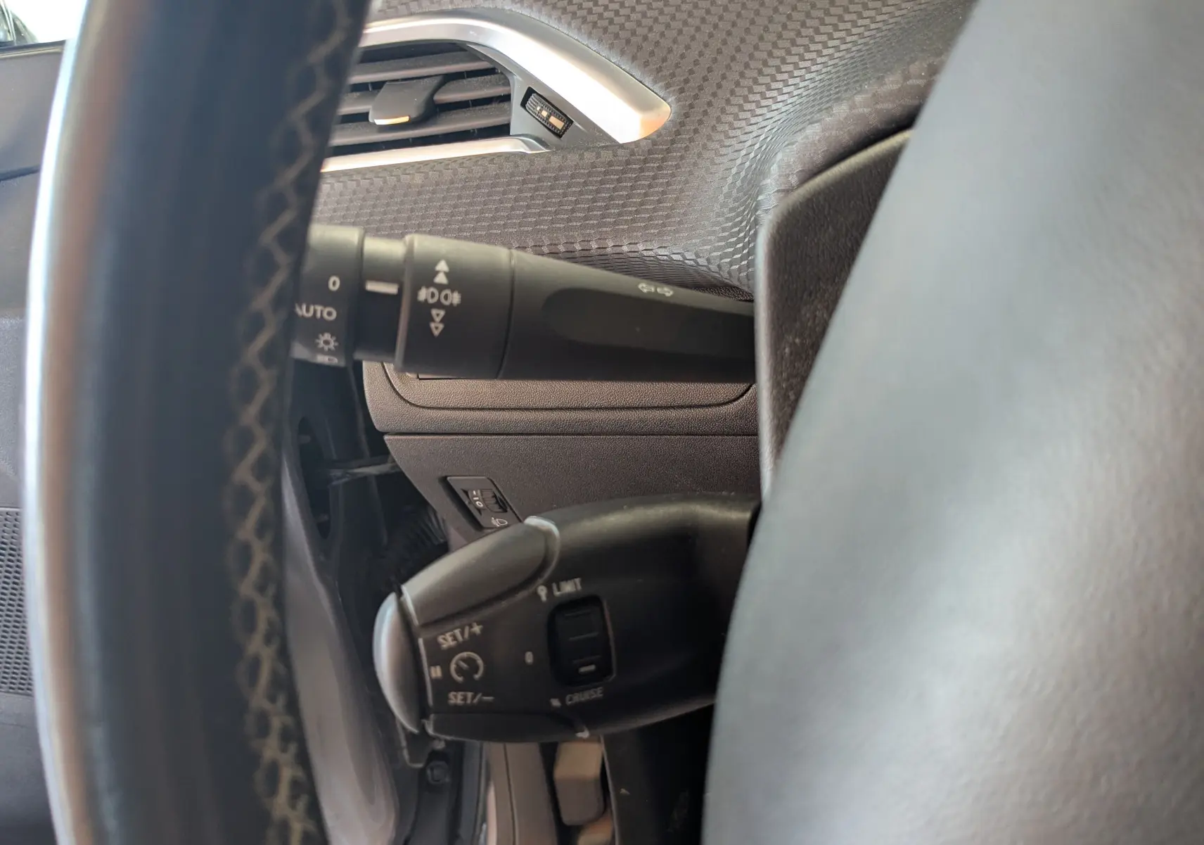 Gros plan sur les commandes au volant côté gauche du Peugeot 2008 gris artense, mettant en valeur les fonctions régulateur et éclairage.