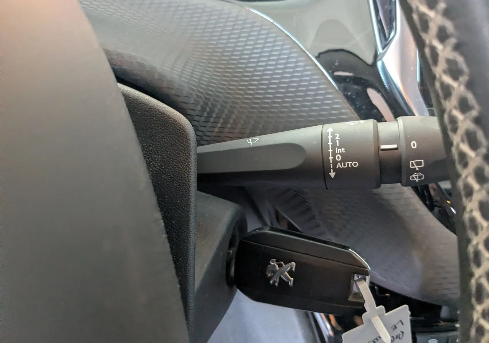 Gros plan sur la commande d'essuie-glace et la clé insérée dans le contacteur d'un Peugeot 2008 gris Artense, intérieur noir.