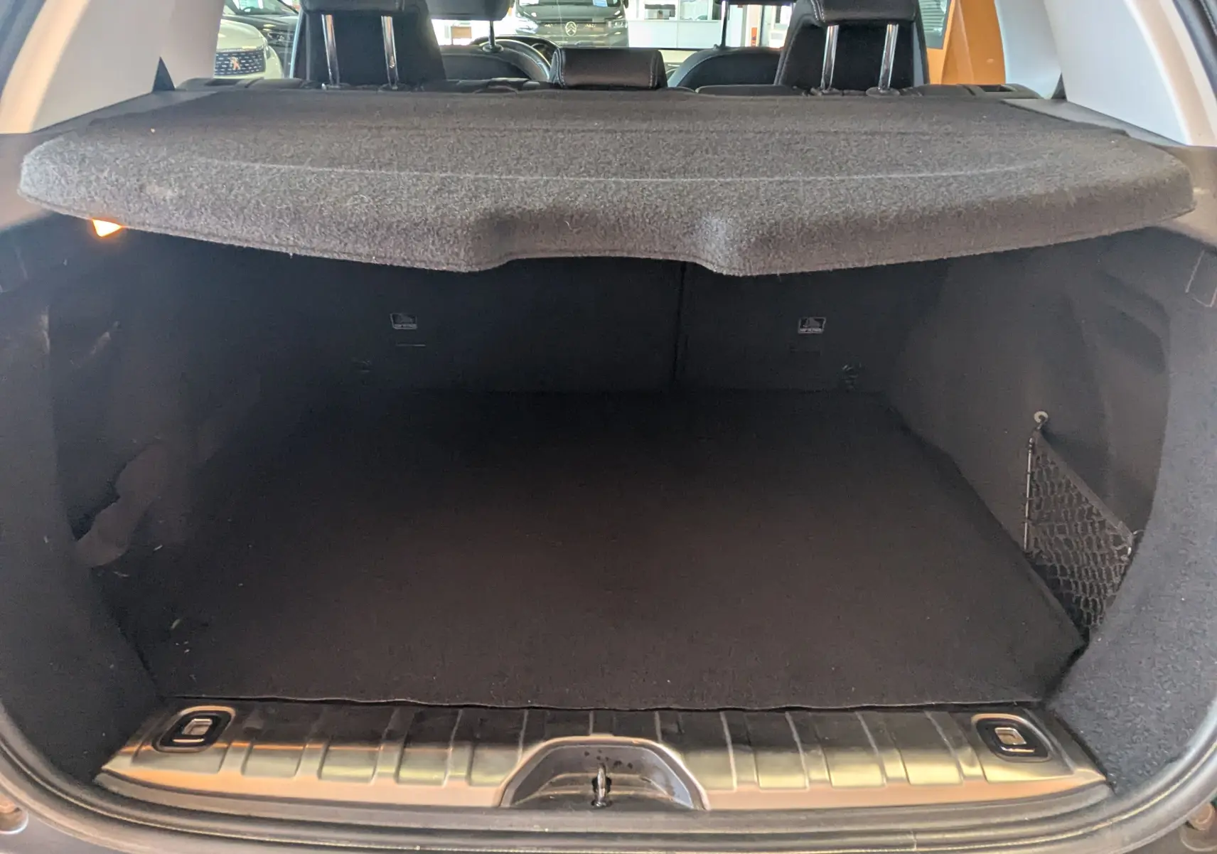 Coffre ouvert vu de l'arrière d'un Peugeot 2008 gris artense, avec cache-bagages en place et intérieur noir.