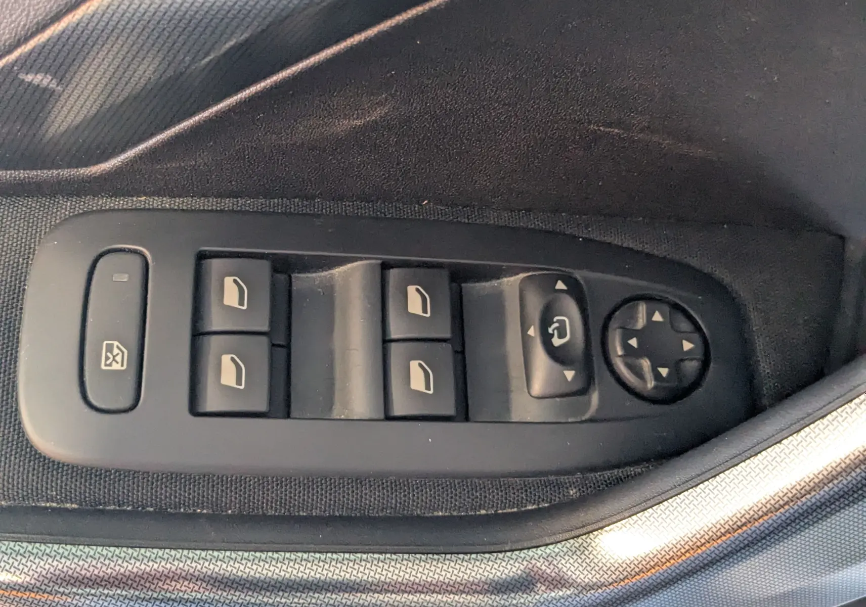 Gros plan sur les commandes électriques des vitres et rétroviseurs côté conducteur d’une Peugeot 2008 gris Artense.