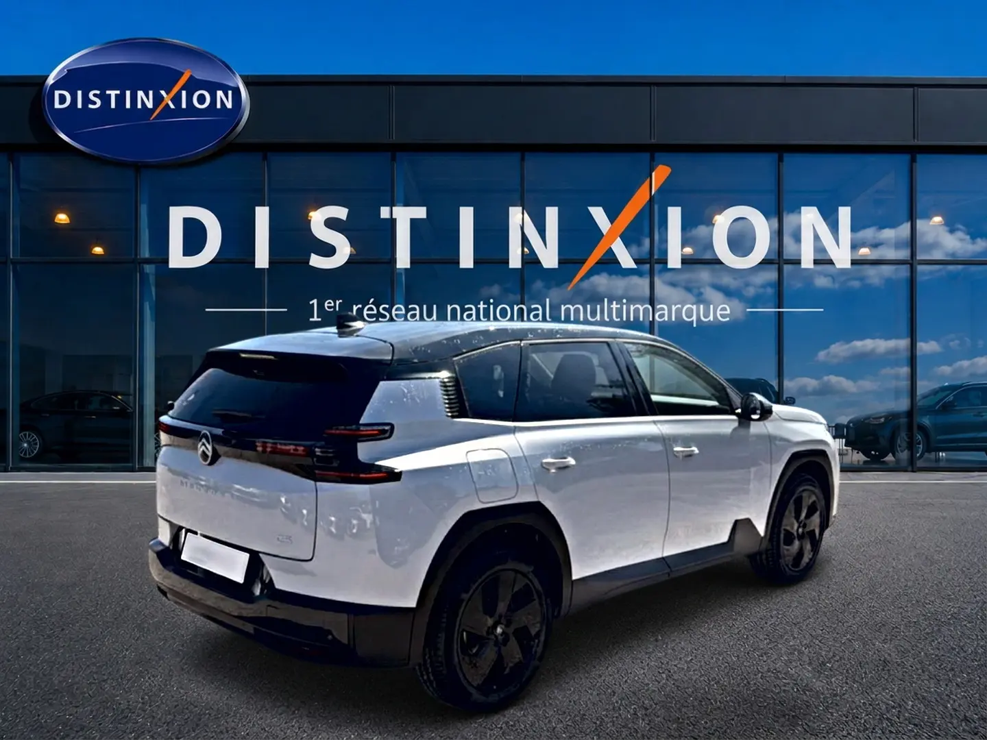 Vue 3/4 arrière droite du Citroën C5 Aircross blanc à toit noir avec jantes alliage noires devant une vitrine Distinxion.