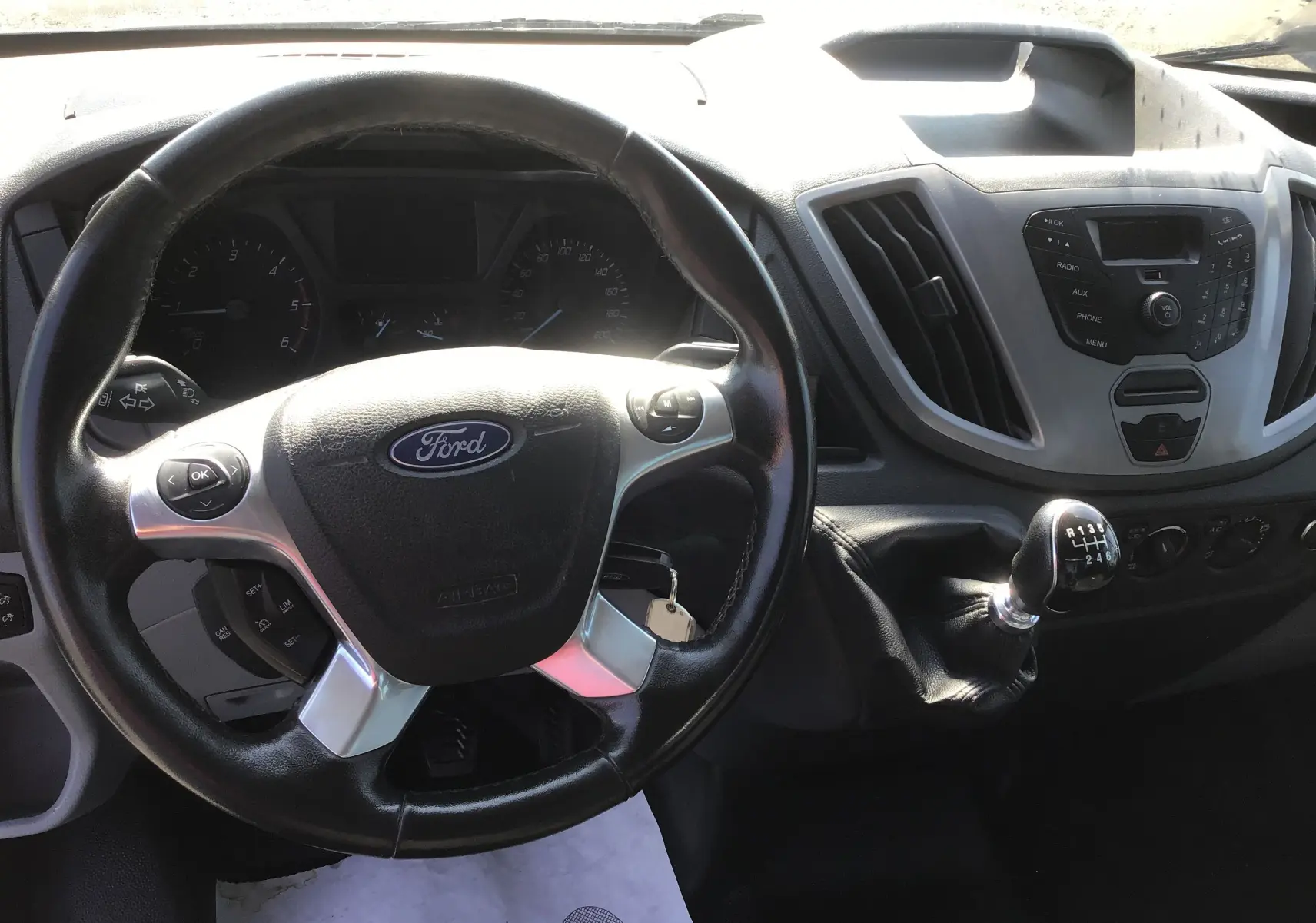 Vue intérieure du tableau de bord du Ford Transit Chassis Cabine blanc, volant cuir et levier de vitesse manuel visibles.