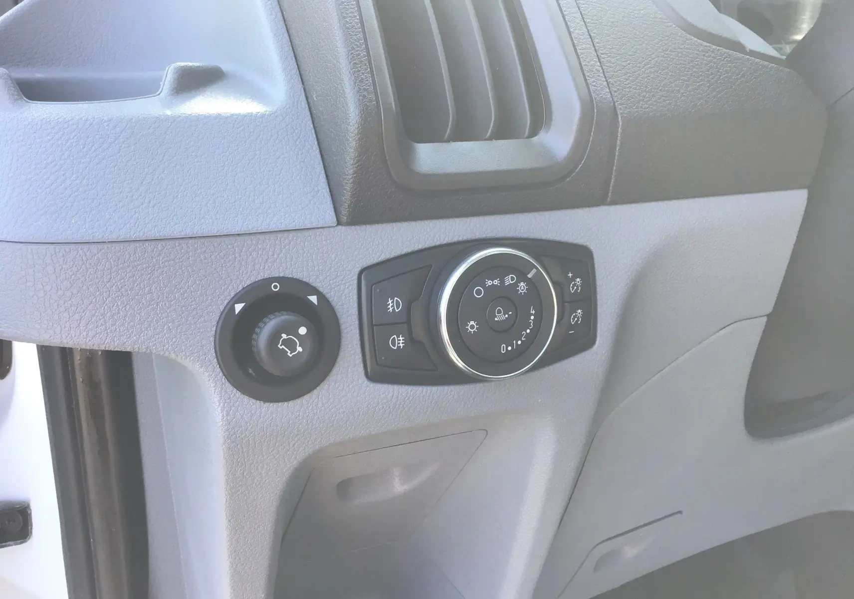 Vue rapprochée des commandes d’éclairage sur la planche de bord grise du Ford Transit Châssis Cabine blanc.