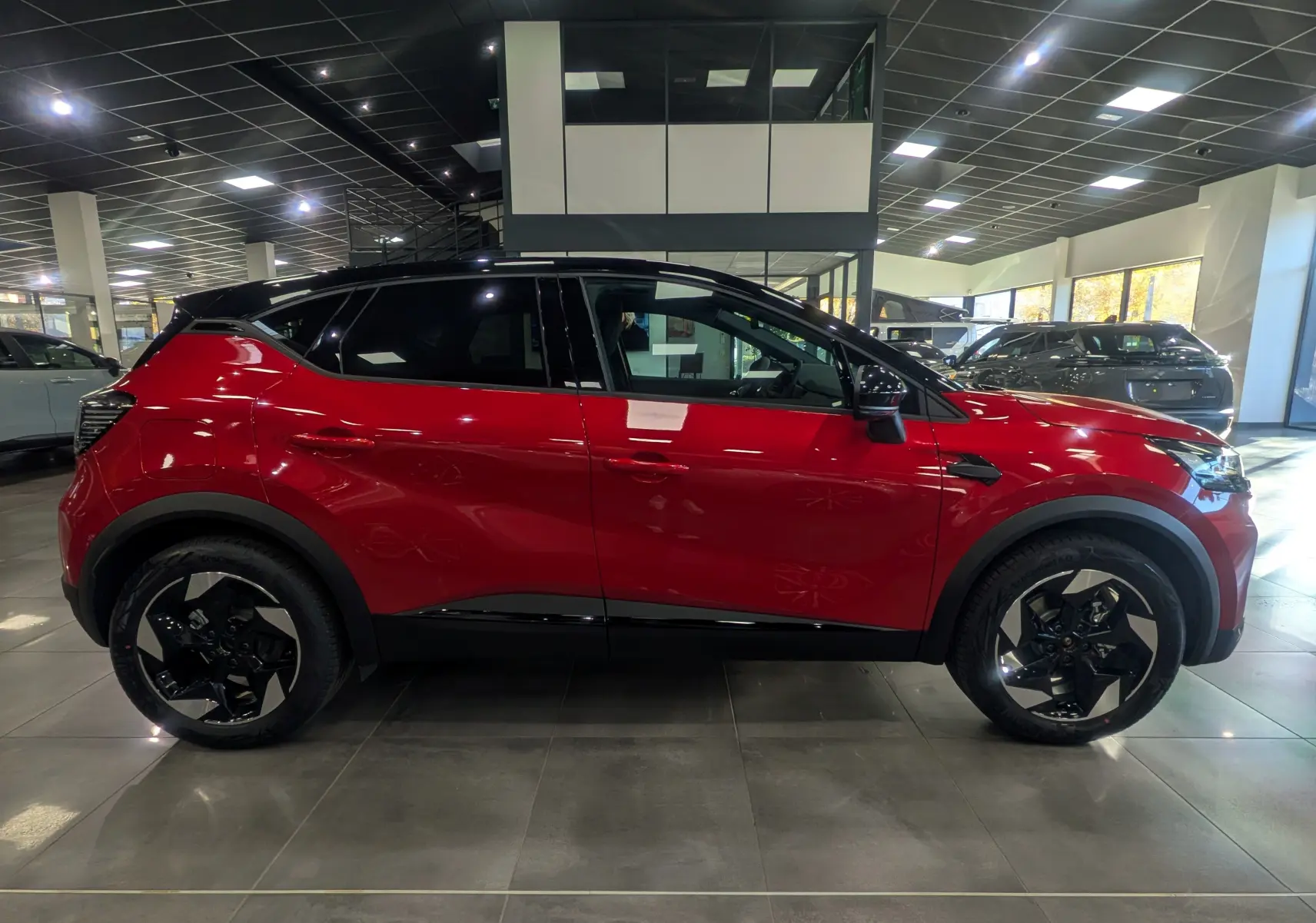 Profil côté gauche du Renault Captur E-TECH rouge Flamme avec toit noir et jantes noires en showroom.