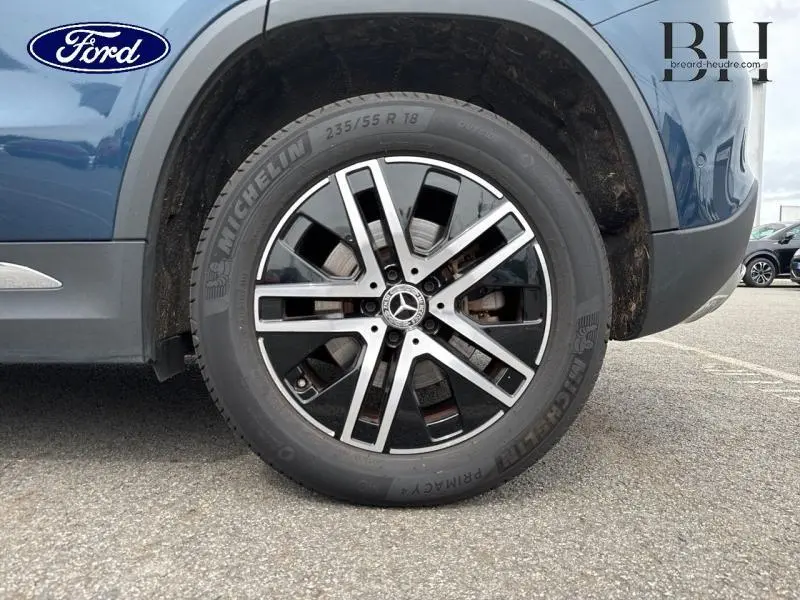 Gros plan sur la roue avant droite bleu denim métallisé du Mercedes GLA 250 e avec jante alliage et logo étoile central.