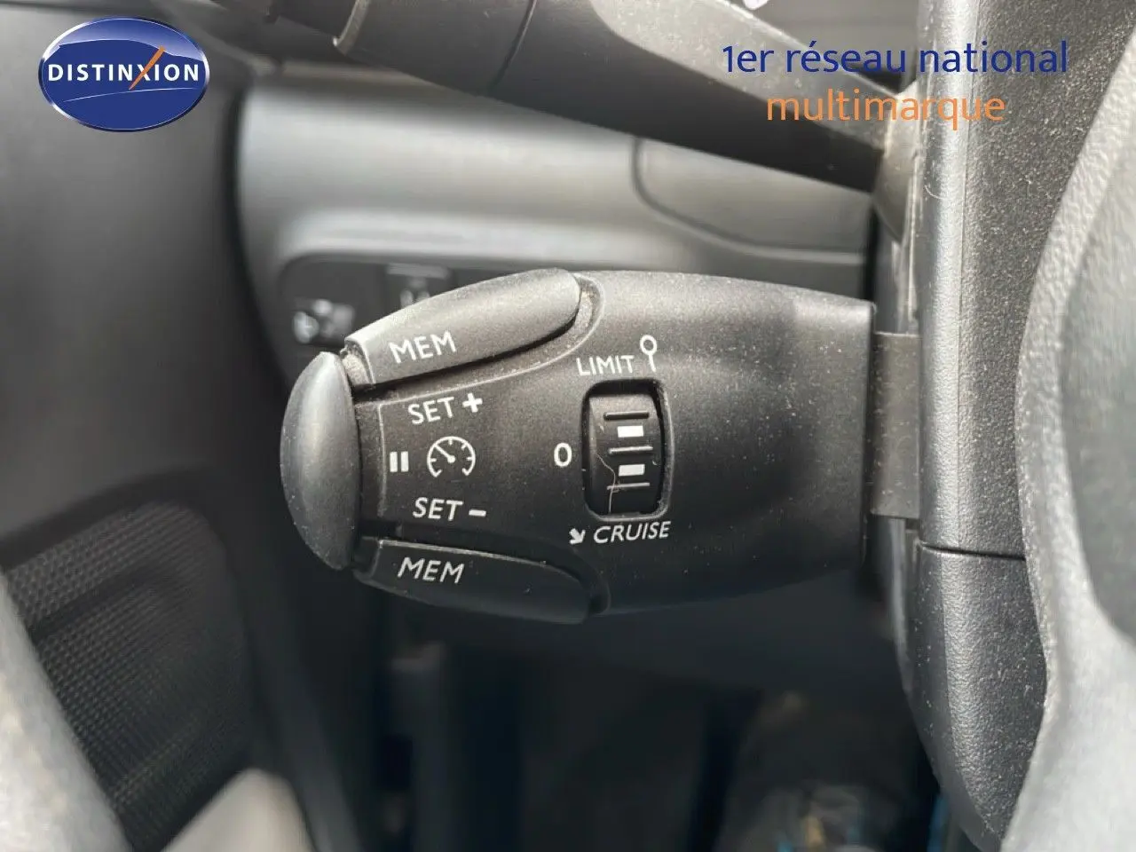 Gros plan sur la commande de régulateur de vitesse à gauche du volant d'une Citroën C3 blanc toit rouge, intérieur noir.