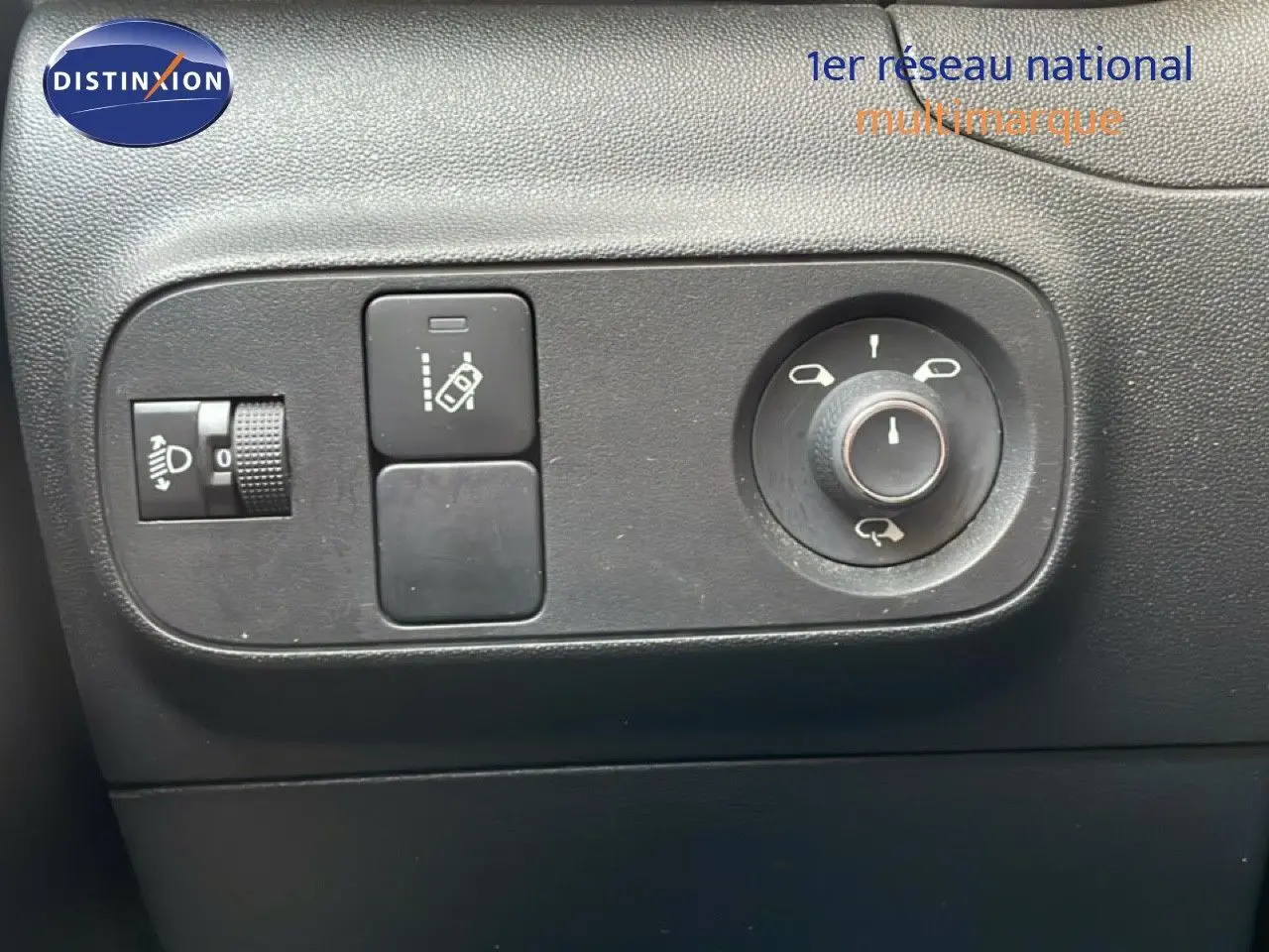 Gros plan sur les commandes de réglage des rétroviseurs et des phares d’une Citroën C3 blanche toit rouge, intérieur noir.