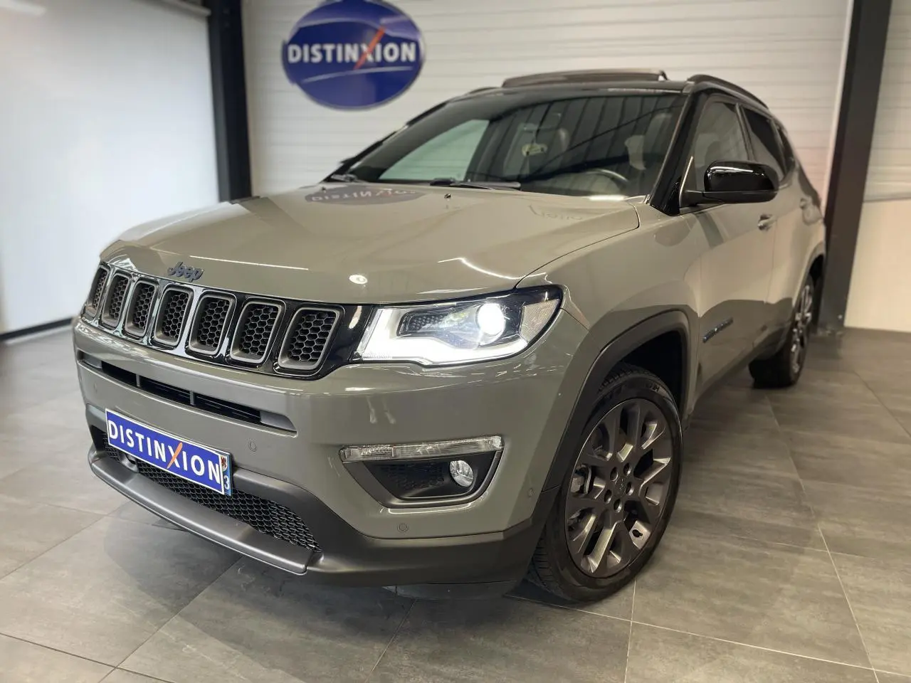 Jeep Compass gris foncé en 3/4 avant droit avec phares allumés et jantes alliage 17 pouces en showroom.