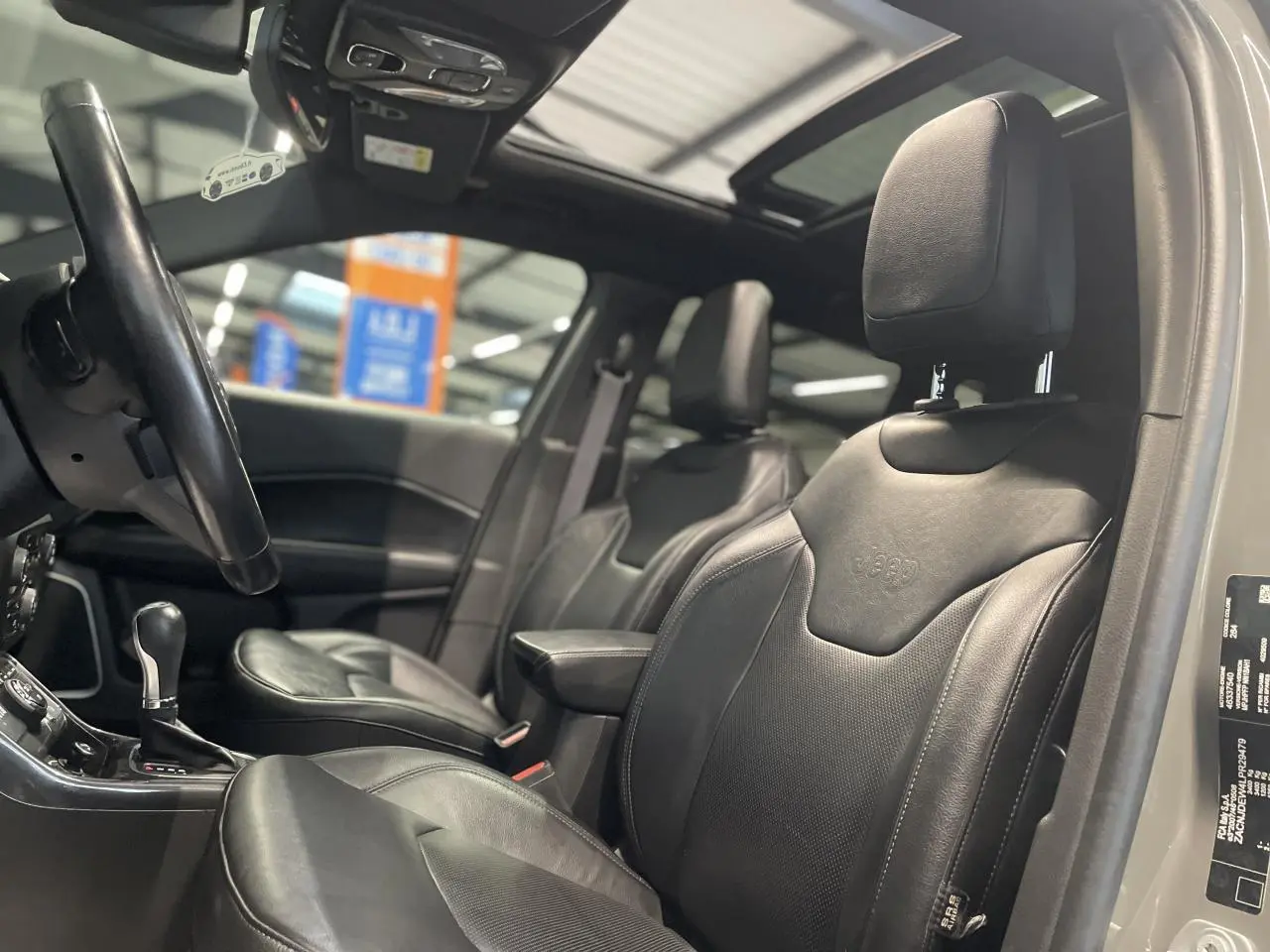 Vue intérieure côté conducteur du Jeep Compass gris foncé, mettant en valeur les sièges cuir noirs et le toit ouvrant panoramique.