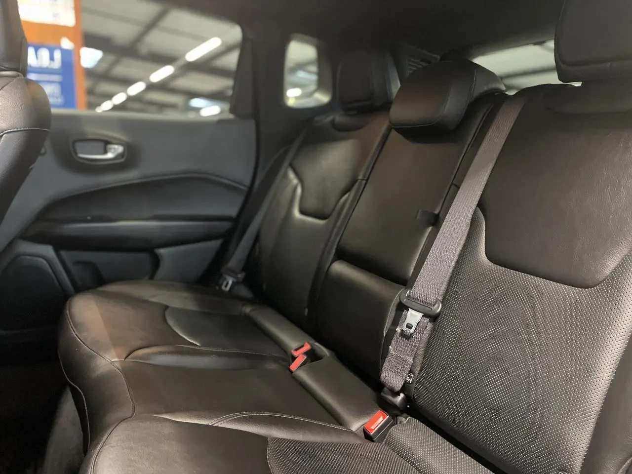 Vue latérale droite de la banquette arrière en cuir noir du Jeep Compass avec ceinture de sécurité grise visible.