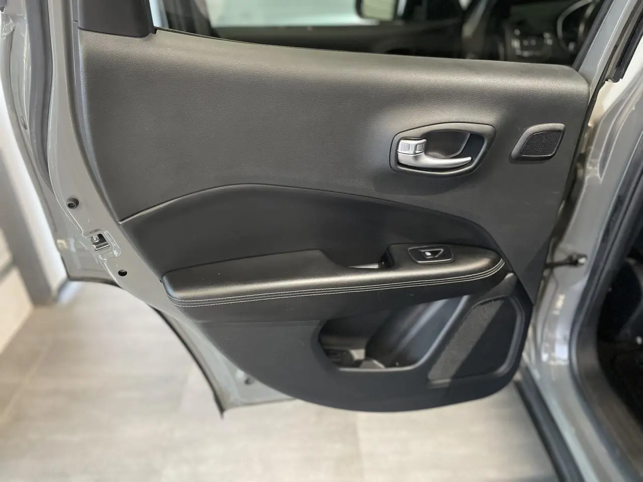 Vue rapprochée de la porte arrière droite ouverte d’un Jeep Compass gris foncé, avec garniture intérieure noire.