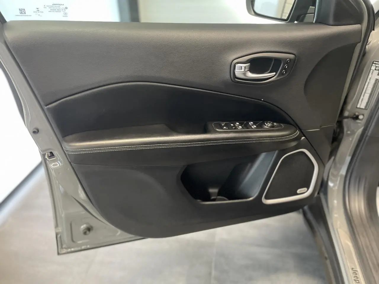 Vue rapprochée de la porte avant gauche gris foncé du Jeep Compass avec commandes électriques et haut-parleur intégré.