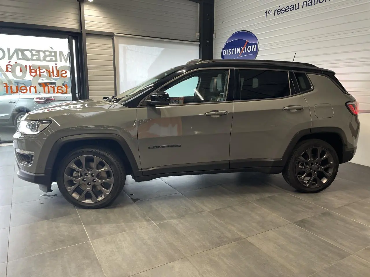 Vue de profil côté gauche d'un Jeep Compass gris foncé avec jantes alliage et vitres arrière surteintées en intérieur showroom.
