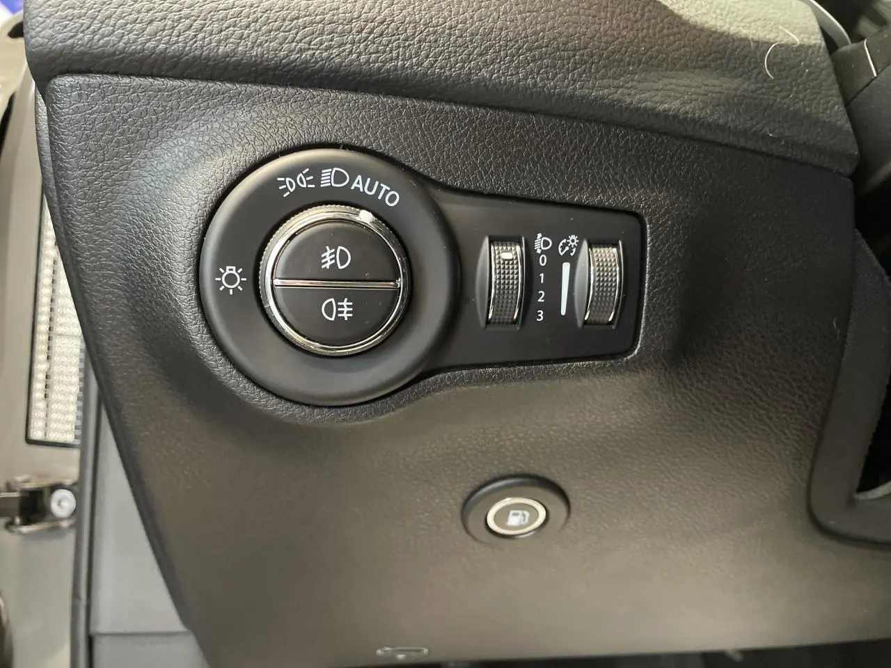 Gros plan sur les commandes d'éclairage et ouverture de trappe à carburant du Jeep Compass gris foncé, intérieur noir.