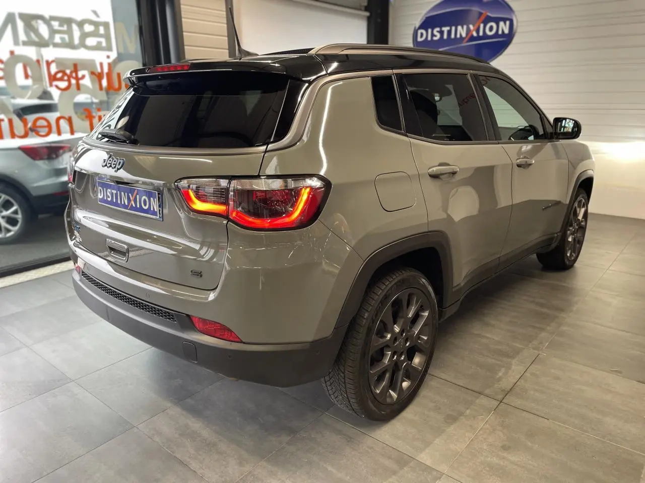 Vue 3/4 arrière droit d'un Jeep Compass gris foncé avec feux arrière allumés et toit noir en intérieur showroom.