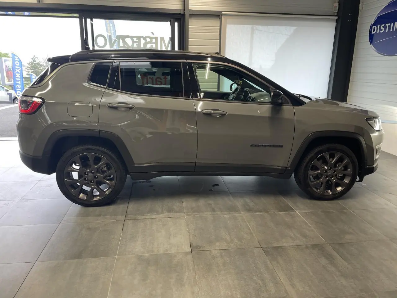 Vue de profil côté gauche d’un Jeep Compass gris foncé avec jantes alliage et vitres surteintées en intérieur showroom.