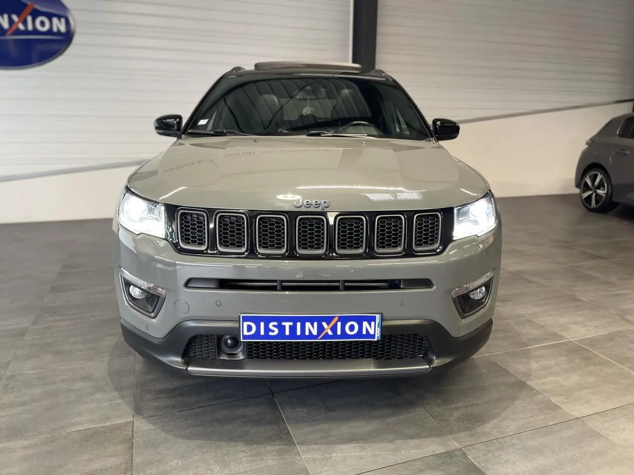Vue avant d'un Jeep Compass gris foncé avec calandre à sept fentes et phares LED allumés en intérieur showroom.