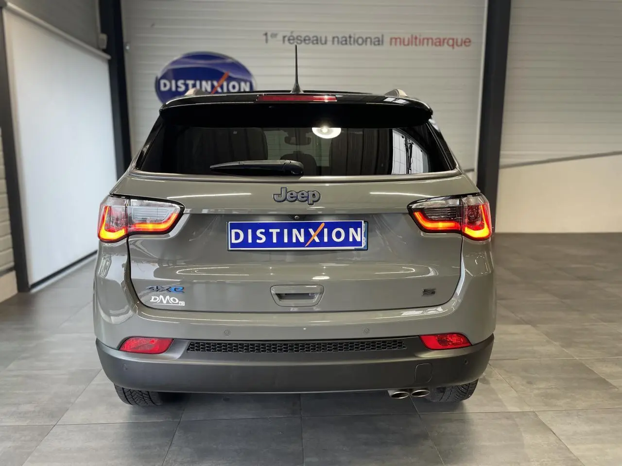 Vue arrière d'un Jeep Compass gris foncé avec feux allumés et double sortie d'échappement visible en intérieur showroom.