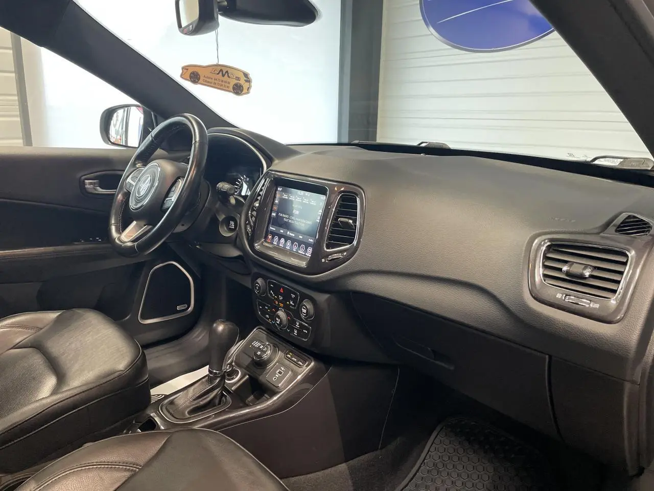 Intérieur avant droit du Jeep Compass gris foncé, avec tableau de bord tactile et sellerie cuir noire.