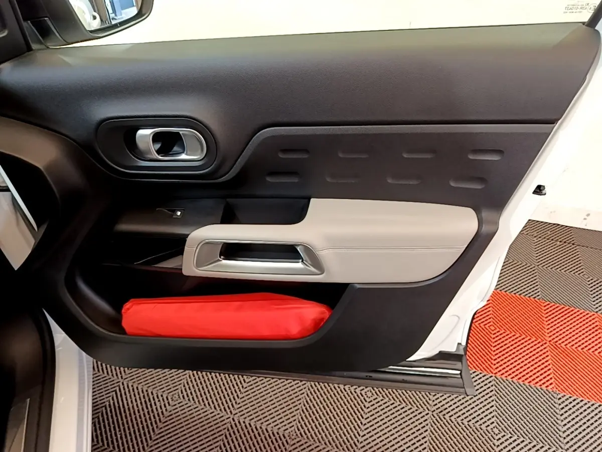 Vue intérieure côté gauche de la porte avant blanche du Citroën C5 Aircross avec garniture noire et beige et rangement rouge.