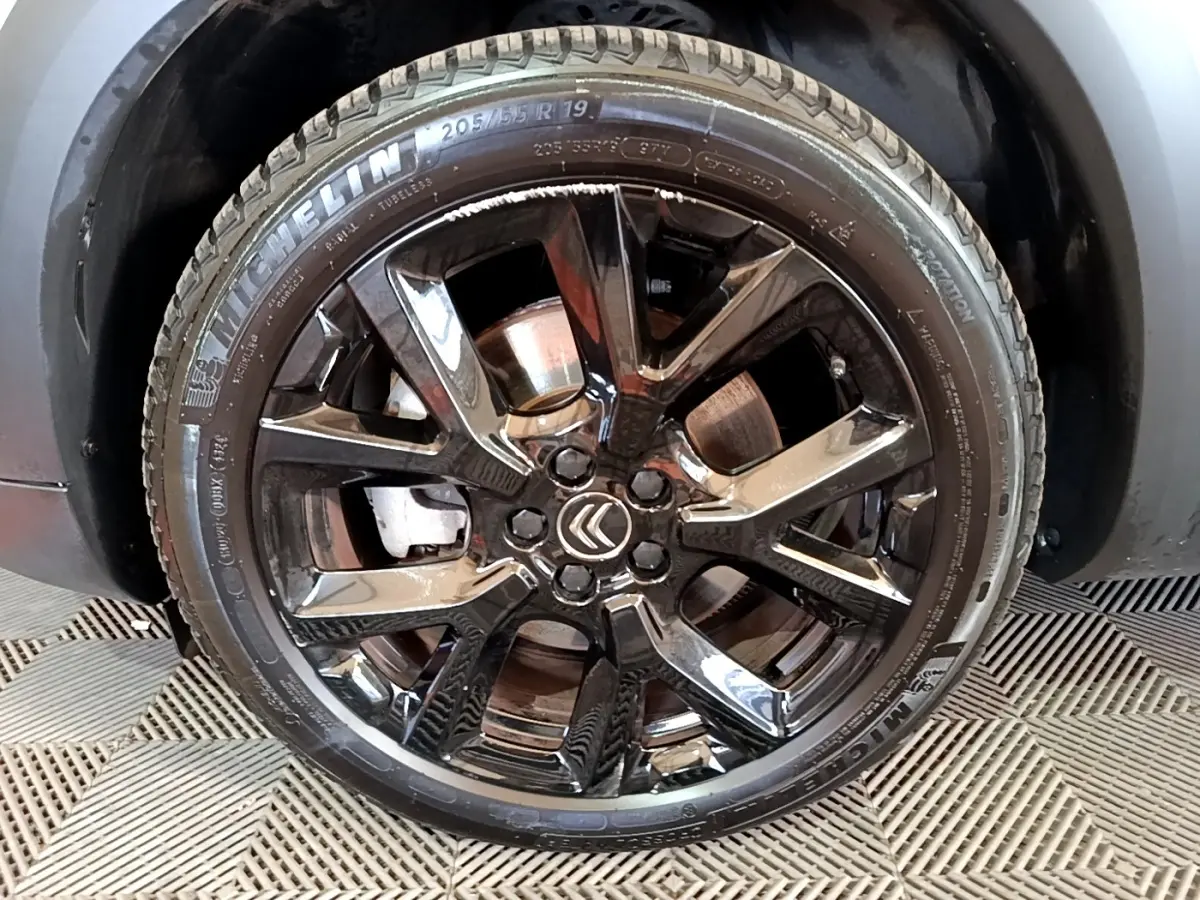 Gros plan sur la roue noire brillante avec logo Citroën, montée sur un Citroën C5 Aircross blanc hybride.