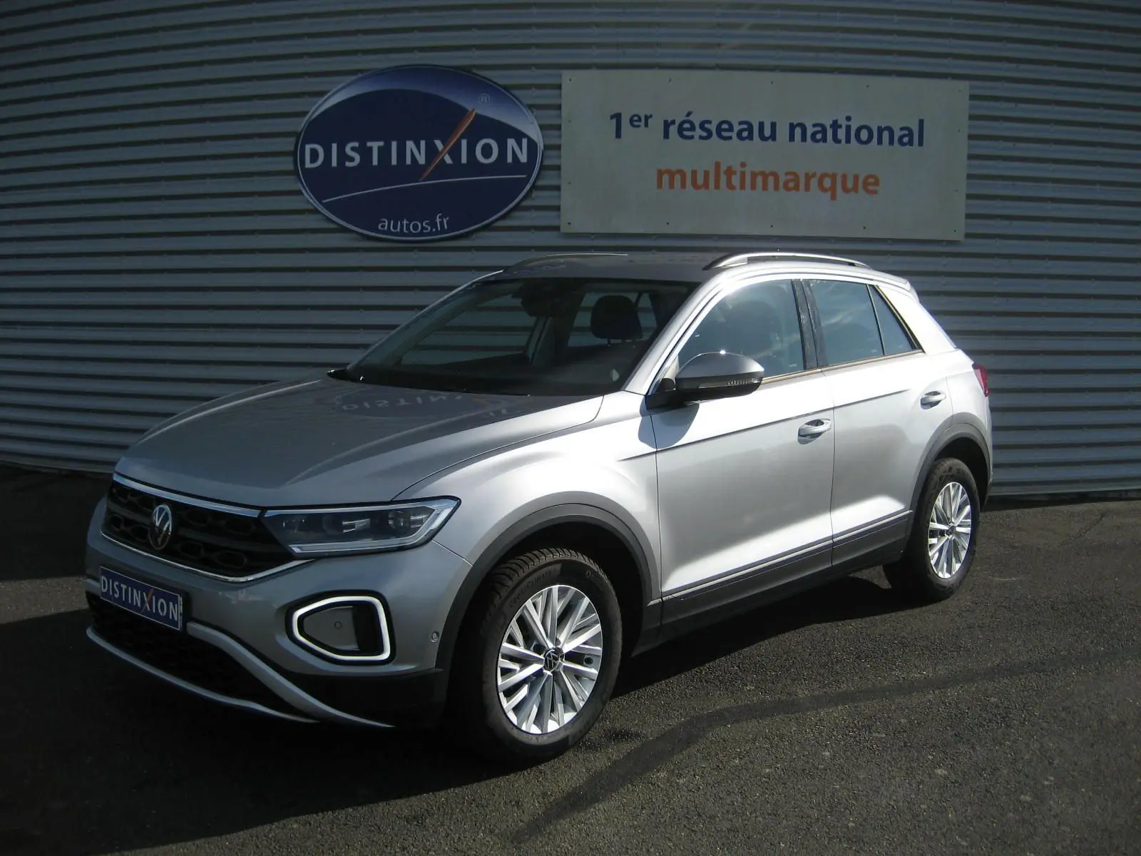 Volkswagen T-Roc gris clair vu en 3/4 avant droit, avec jantes alliage et calandre noire distinctive.