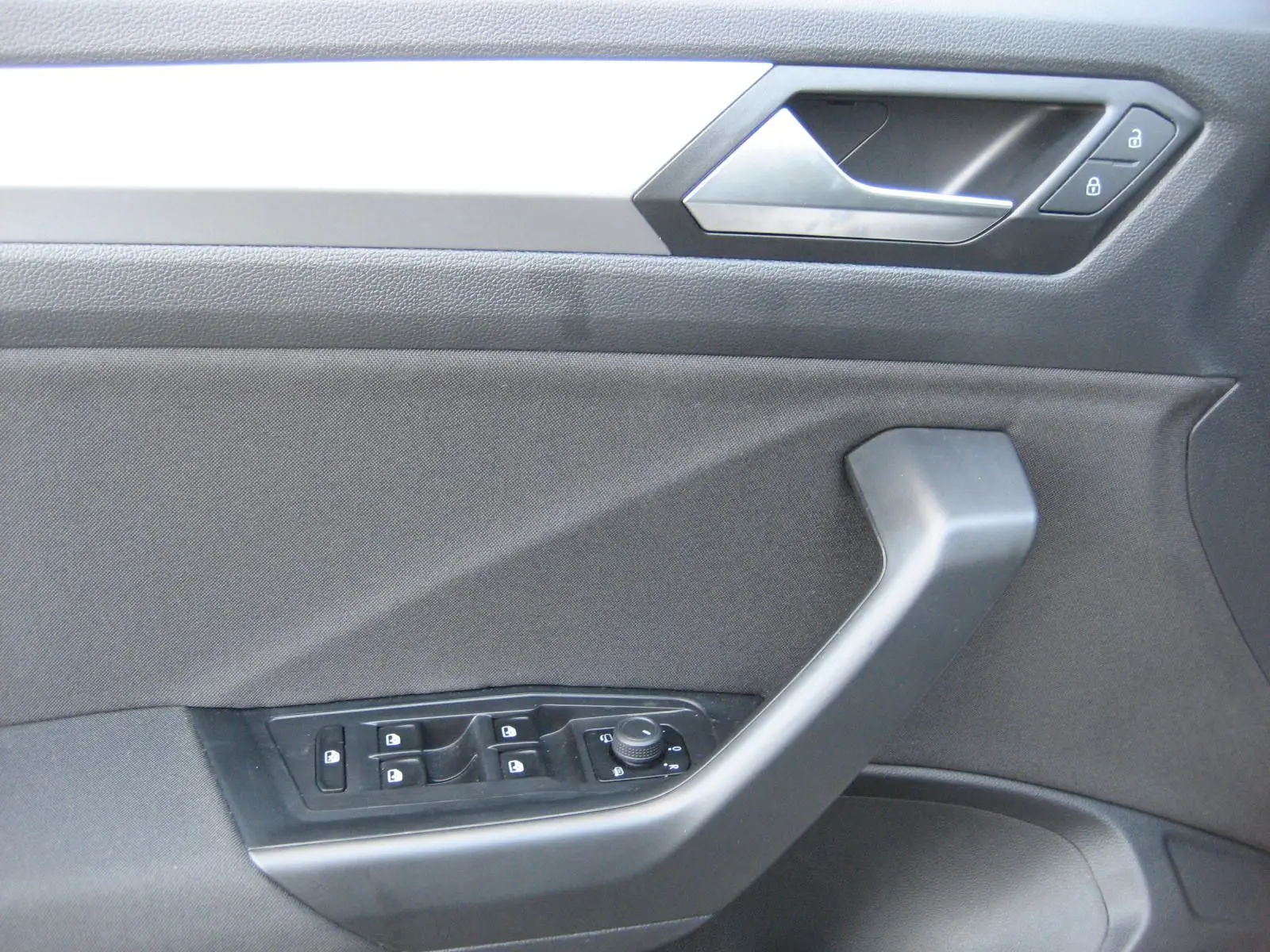 Vue rapprochée de la porte côté gauche du Volkswagen T-Roc gris clair, montrant les commandes des vitres et des rétroviseurs.