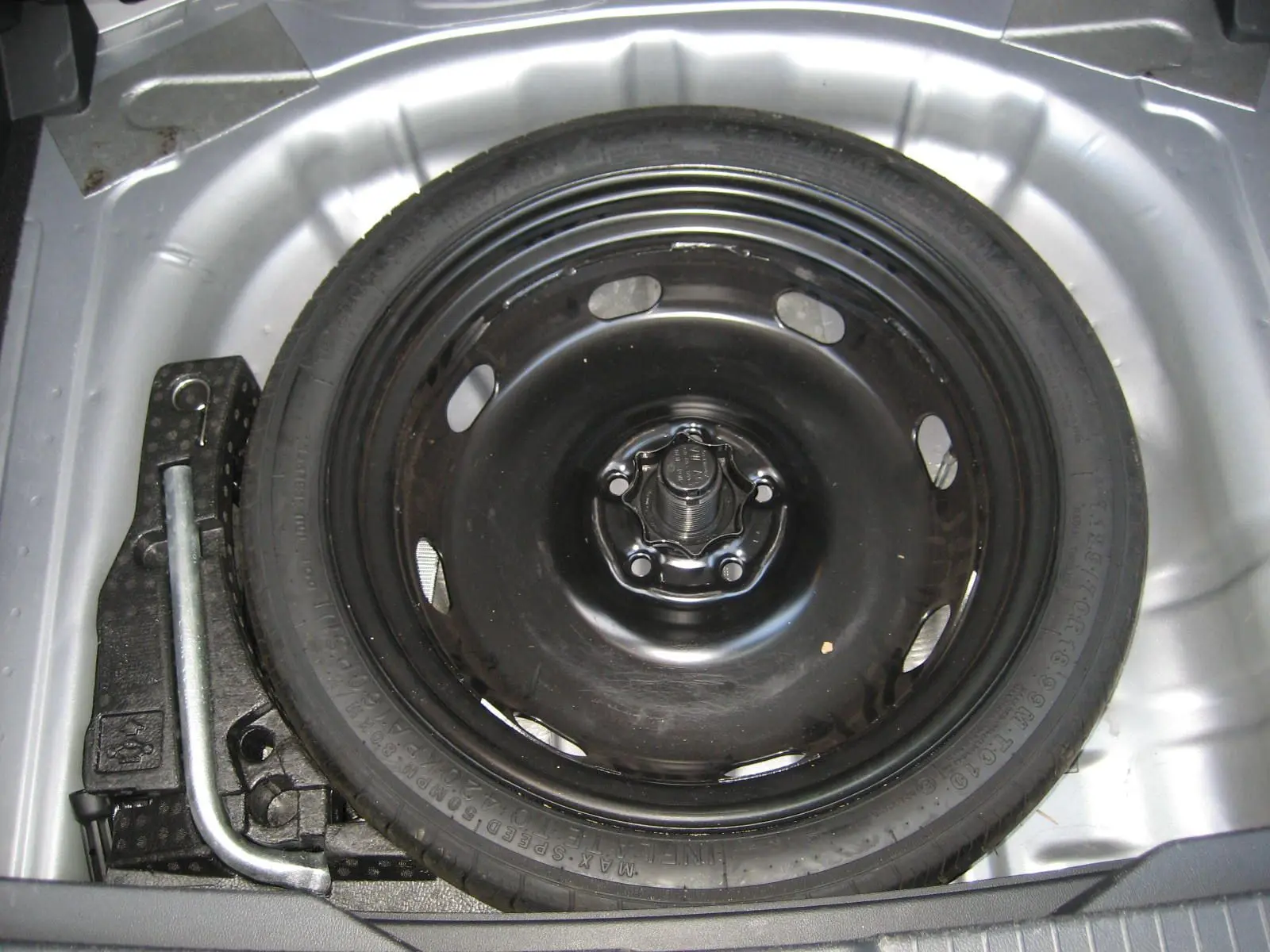 Vue en plongée sur la roue de secours noire et les outils dans le coffre d’un Volkswagen T-Roc gris clair 2023.