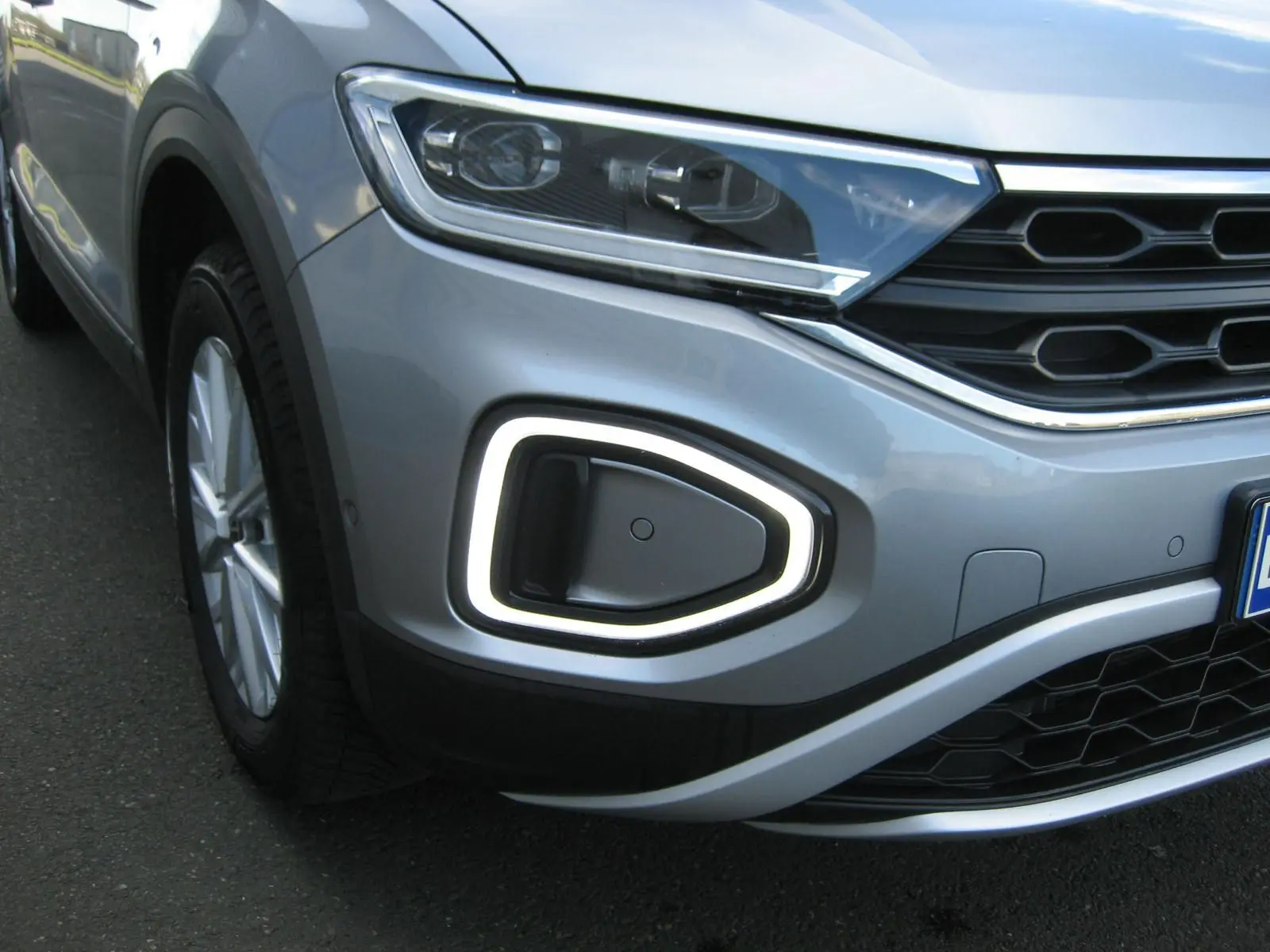 Gros plan sur l’avant droit gris clair du Volkswagen T-Roc 2023, mettant en valeur le phare LED et la signature lumineuse distinctive.