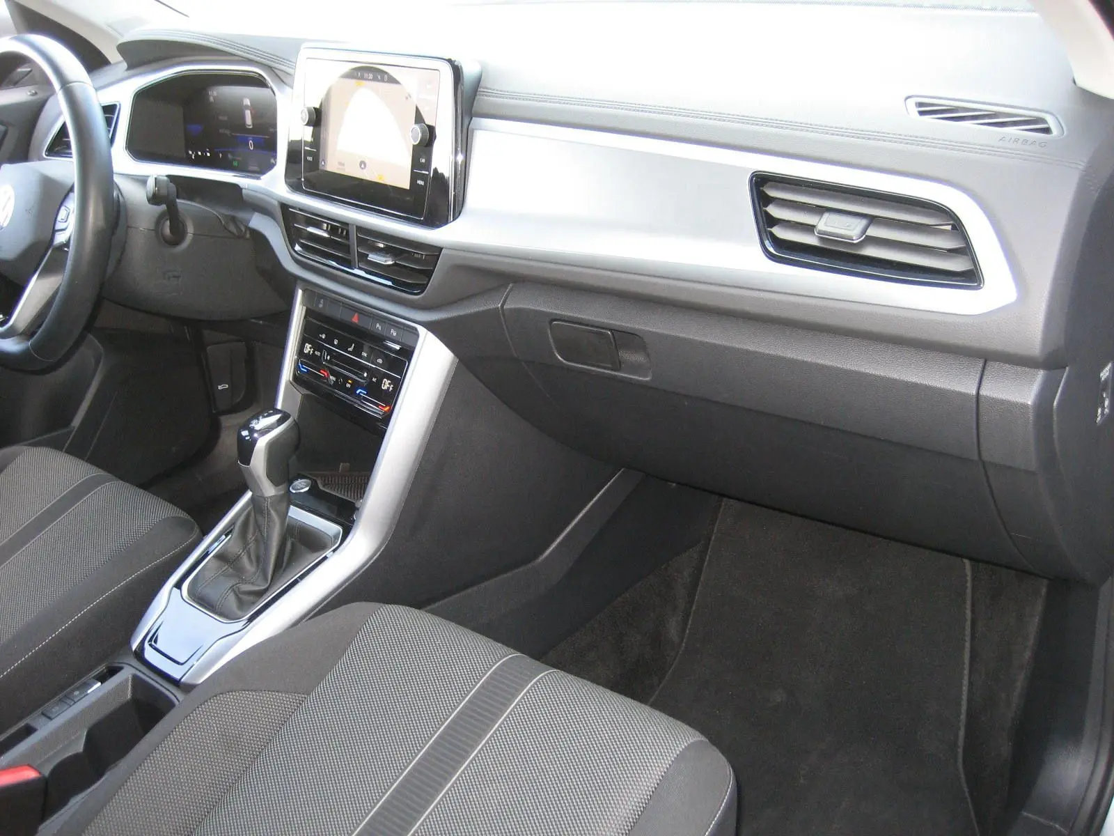 Vue intérieure côté passager du tableau de bord et console centrale du Volkswagen T-Roc 1.5 TSI gris clair avec boîte automatique.
