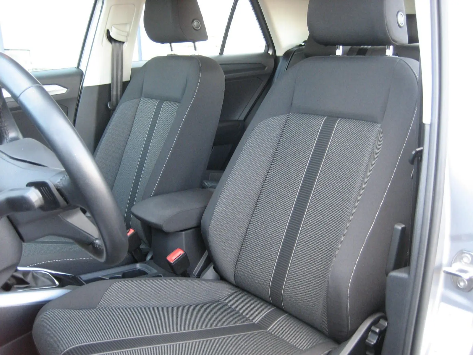 Vue intérieure sur les sièges avant gris foncé du Volkswagen T-Roc 2023, avec accoudoir central et volant partiel visible.