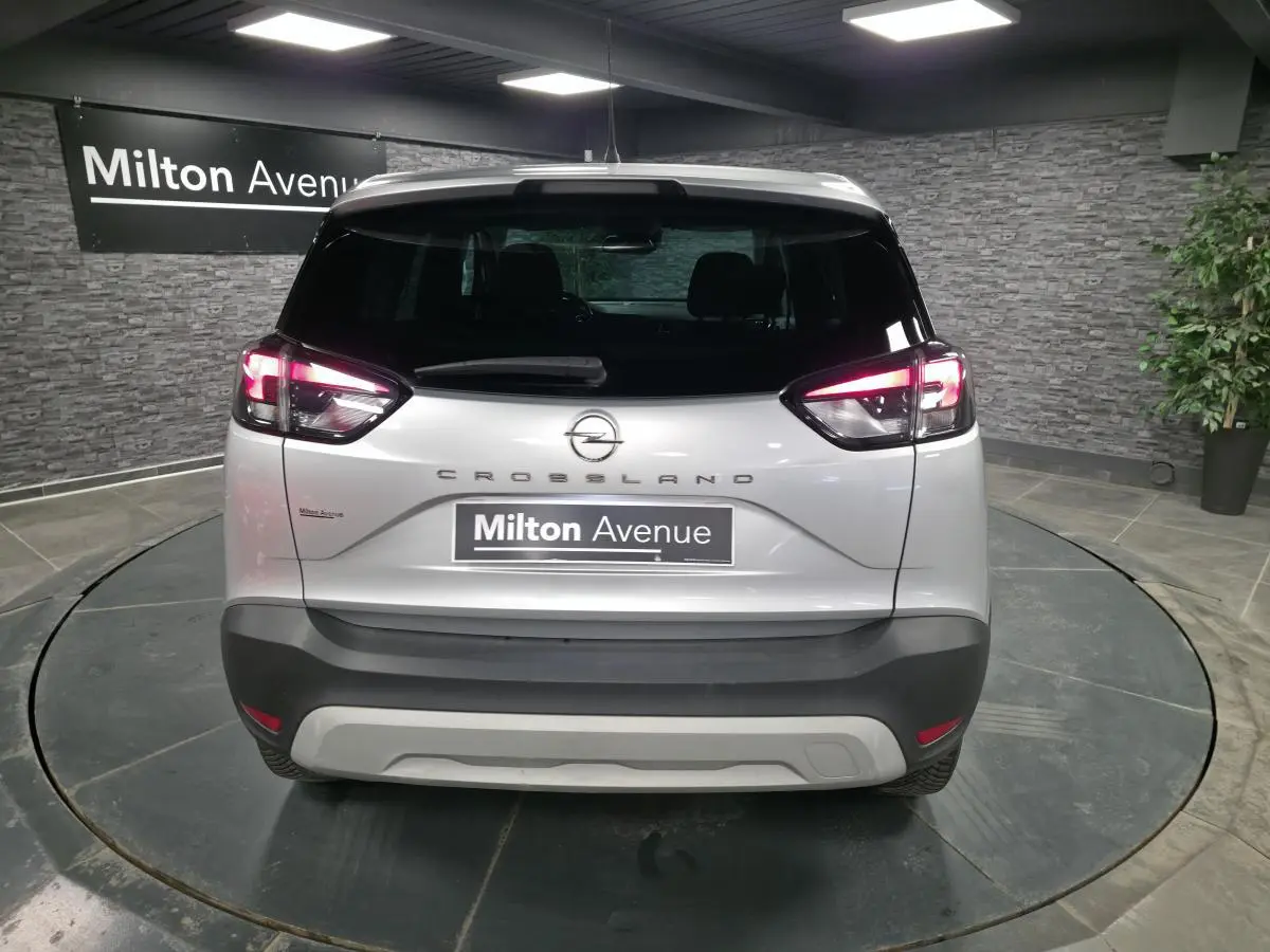 Vue arrière d'un Opel Crossland gris métallisé 2023 avec feux arrière allumés et logo central sur fond intérieur showroom.