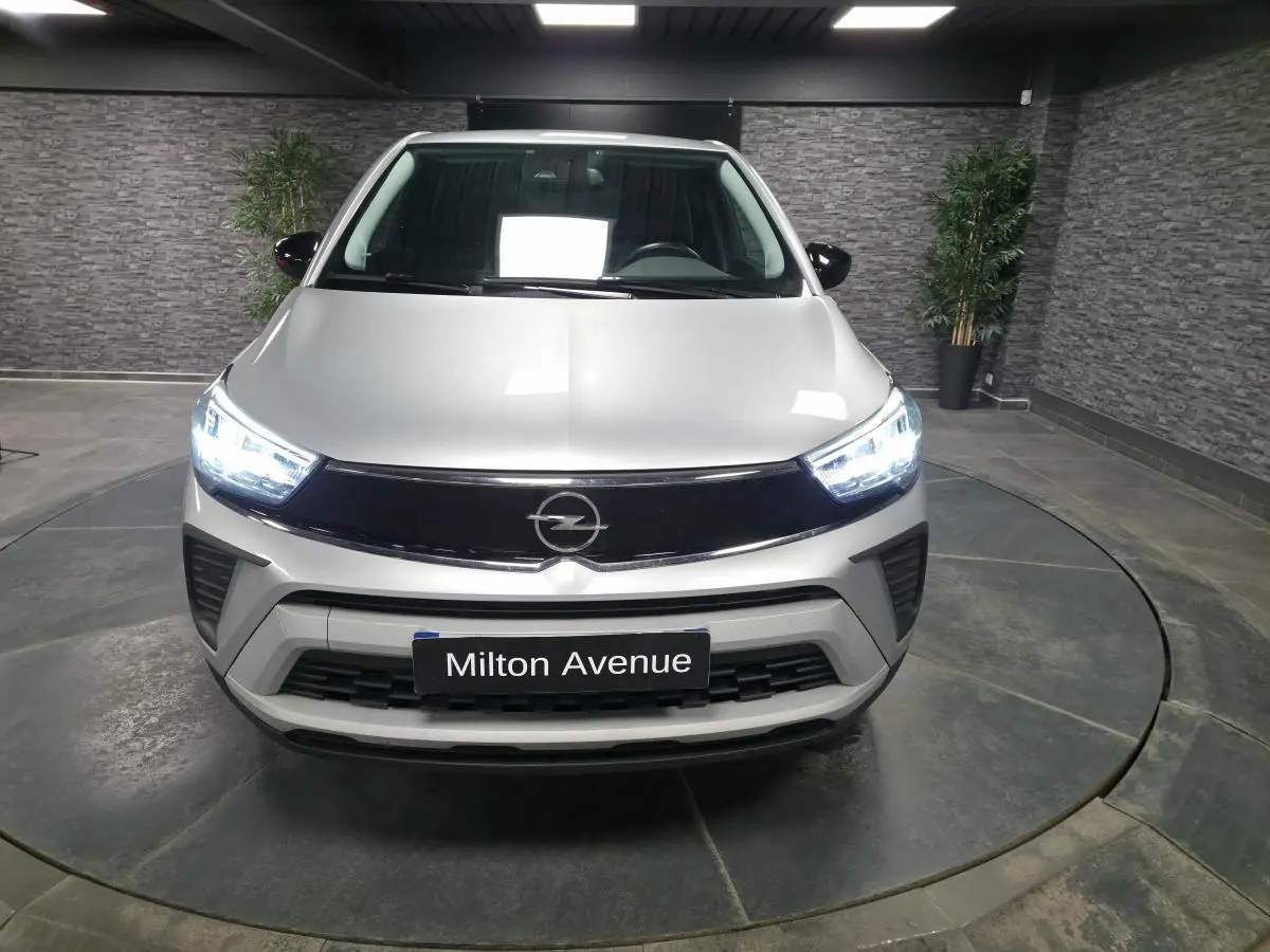 Vue avant d'un Opel Crossland gris métallisé 2023 avec calandre noire et phares LED allumés dans un showroom.