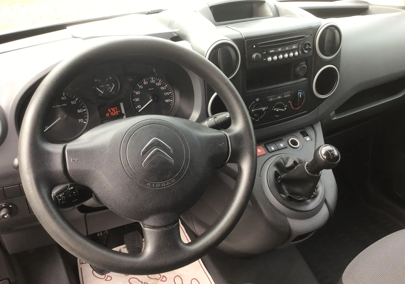 Vue intérieure du poste de conduite du Citroën Berlingo blanc, avec volant, tableau de bord et levier de vitesse manuel visibles.