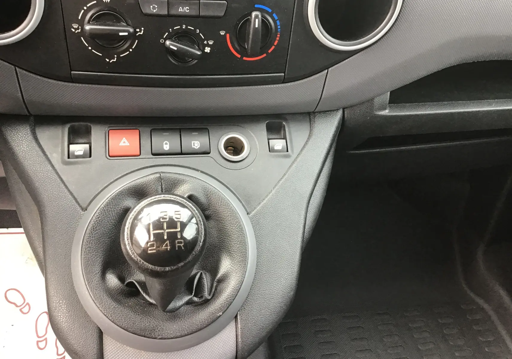Vue rapprochée du levier de vitesses manuel et des commandes de climatisation du Citroën Berlingo blanc de 2018.