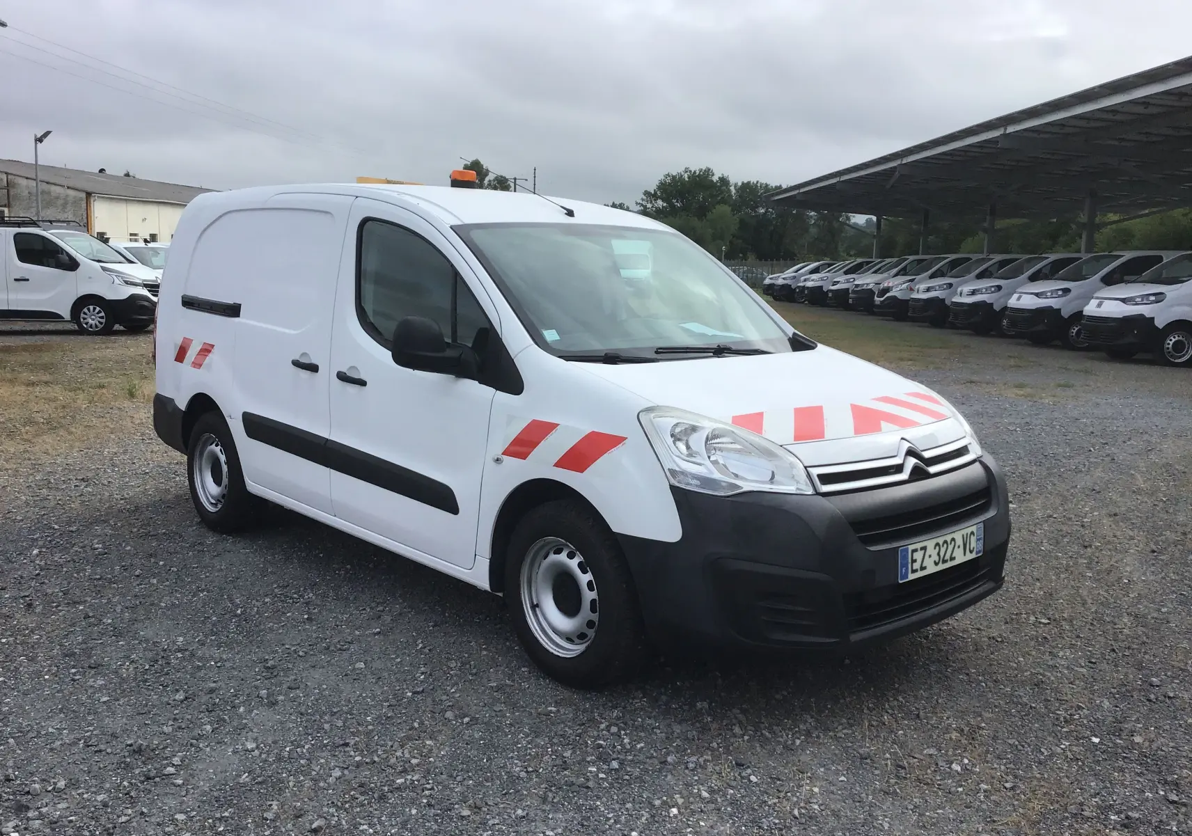 Vue 3/4 avant droite d'un Citroën Berlingo blanc avec bandes rouges réfléchissantes et gyrophare orange sur le toit.