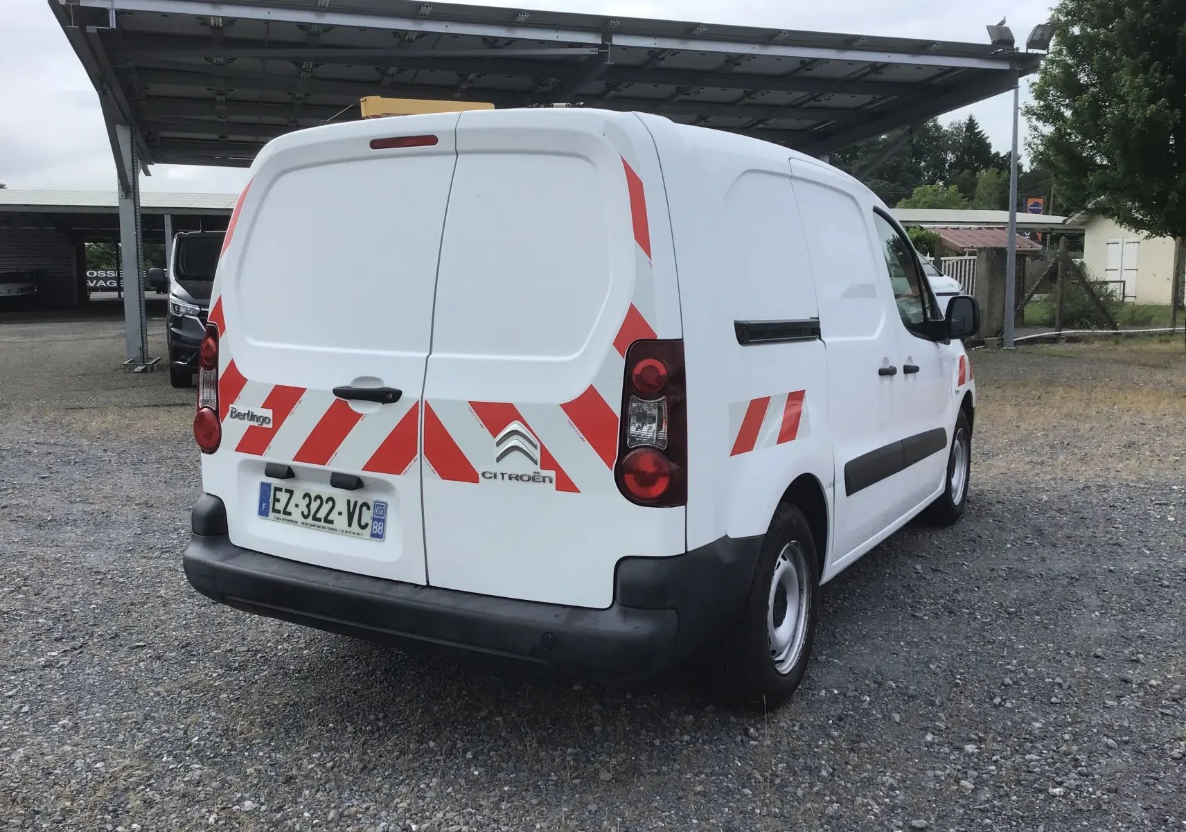 Vue 3/4 arrière droite d'un Citroën Berlingo blanc avec bandes rouges réfléchissantes et plaque d'immatriculation française.