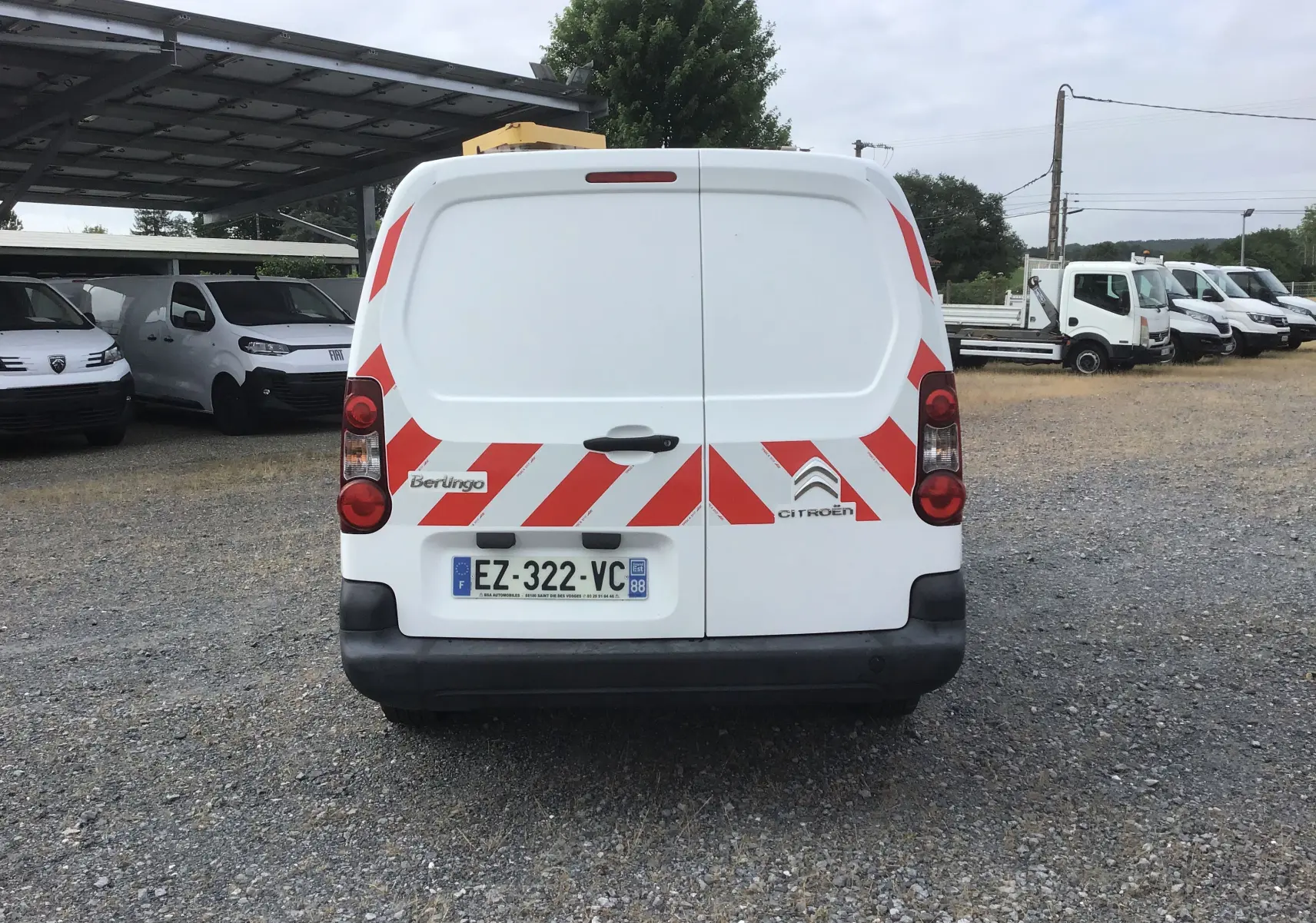 Vue arrière d'un Citroën Berlingo blanc avec bandes rouges réfléchissantes et plaque d'immatriculation française.