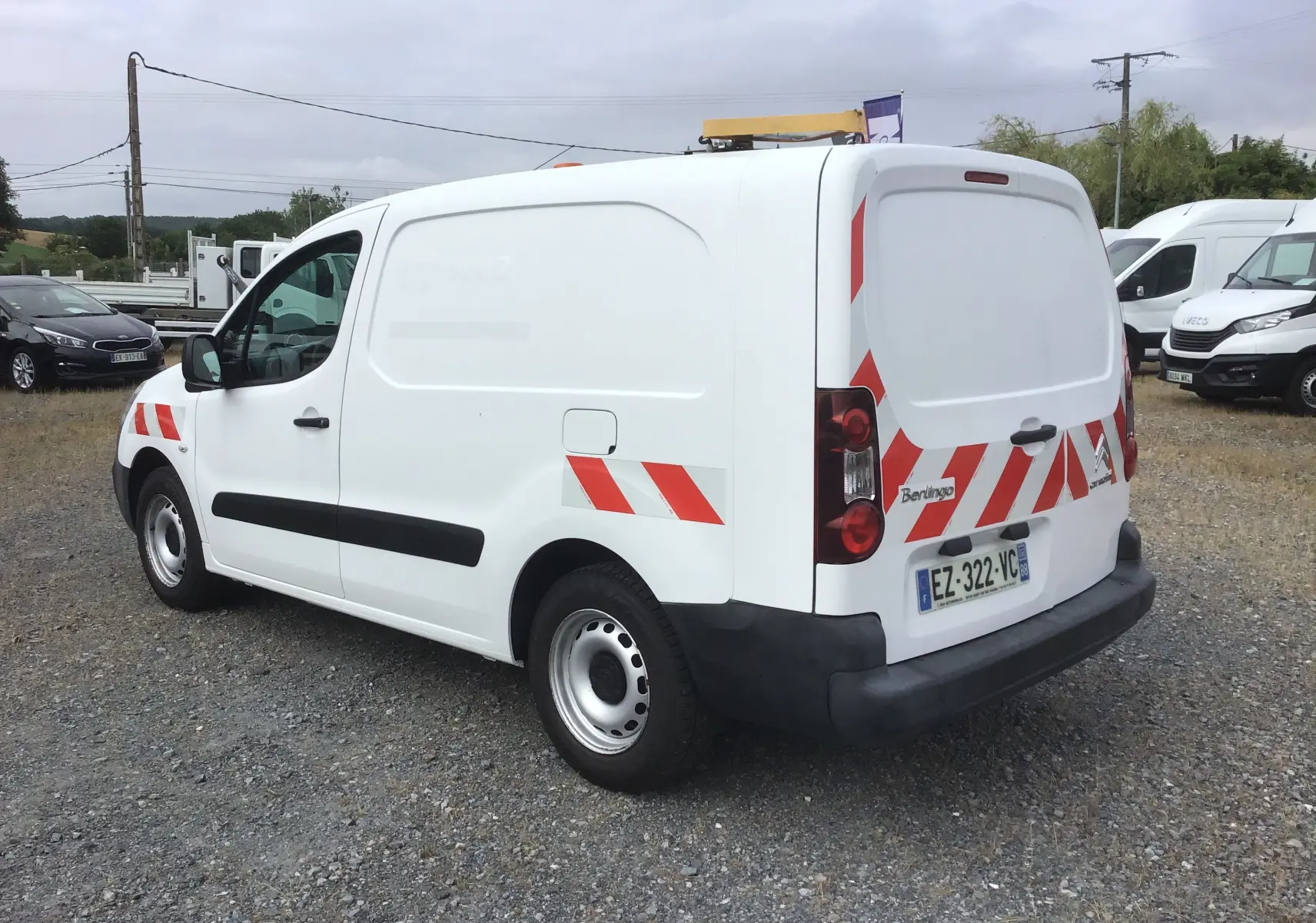 Vue 3/4 arrière droite d’un utilitaire Citroën Berlingo blanc avec bandes réfléchissantes rouges et gyrophare sur le toit.