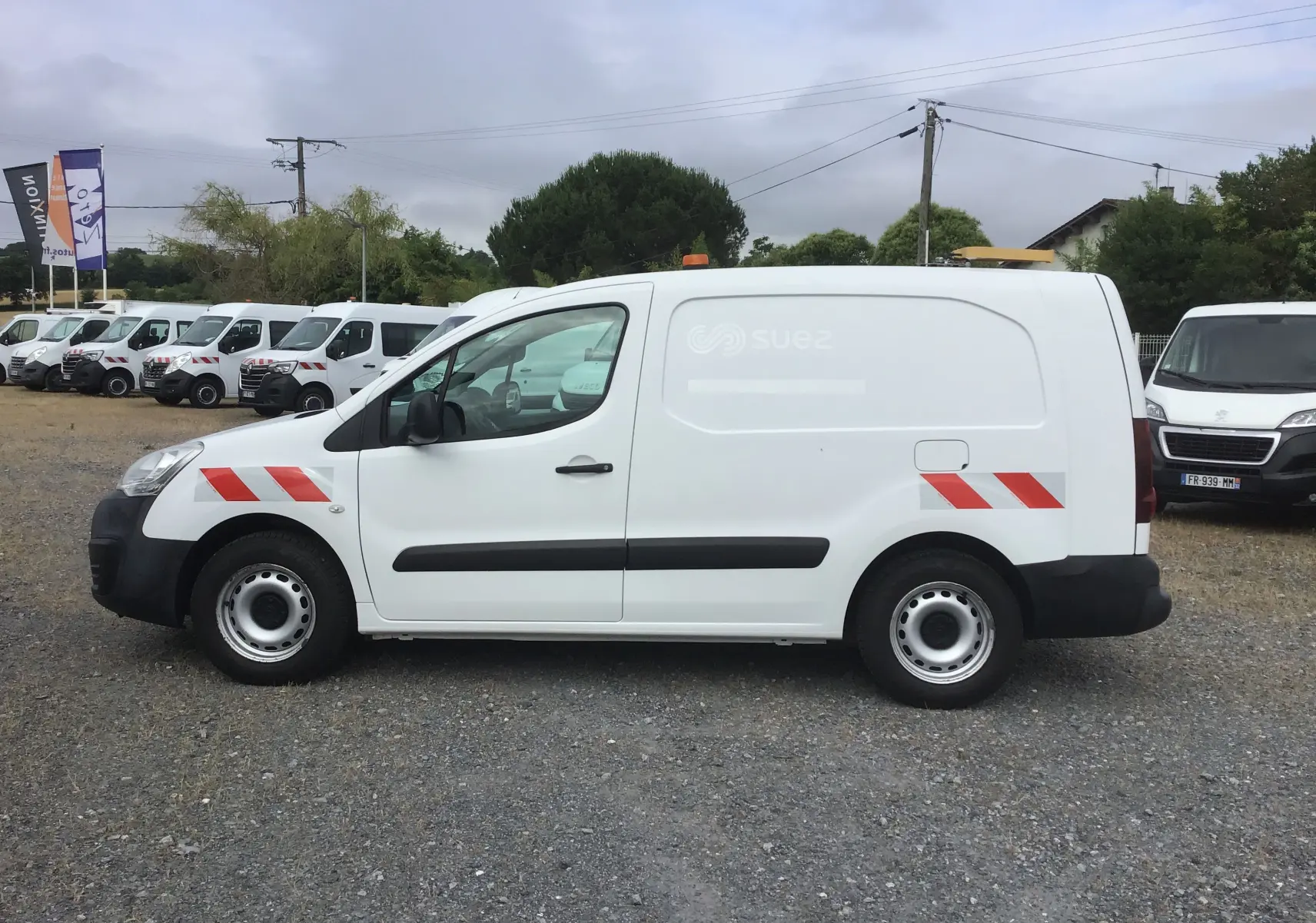 Vue de profil côté gauche d’un Citroën Berlingo XL blanc utilitaire avec bandes rouges diagonales et gyrophare orange sur le toit.